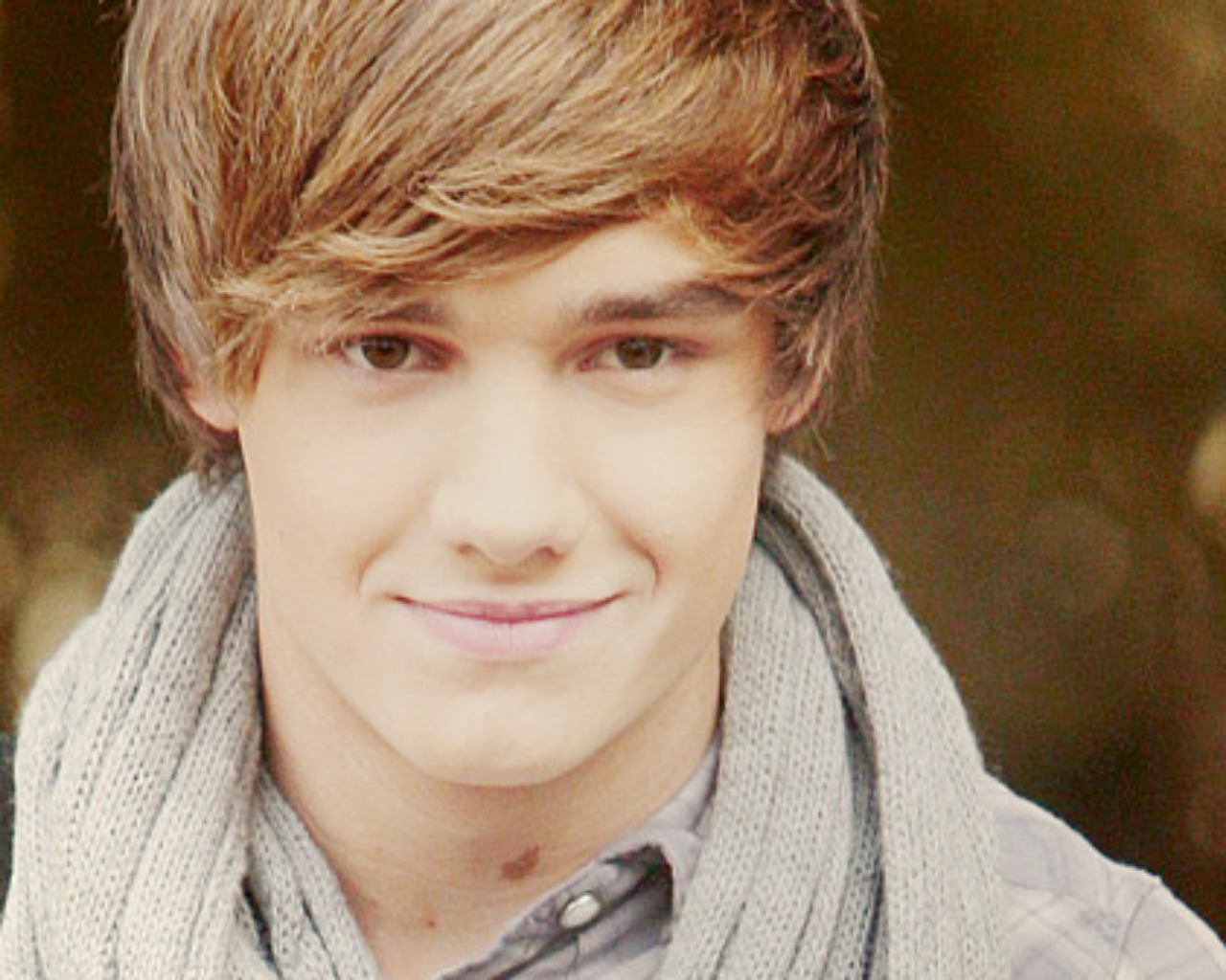 A close-up portrait of a young boy with light brown hair, styled in a layered cut, wearing a gray scarf