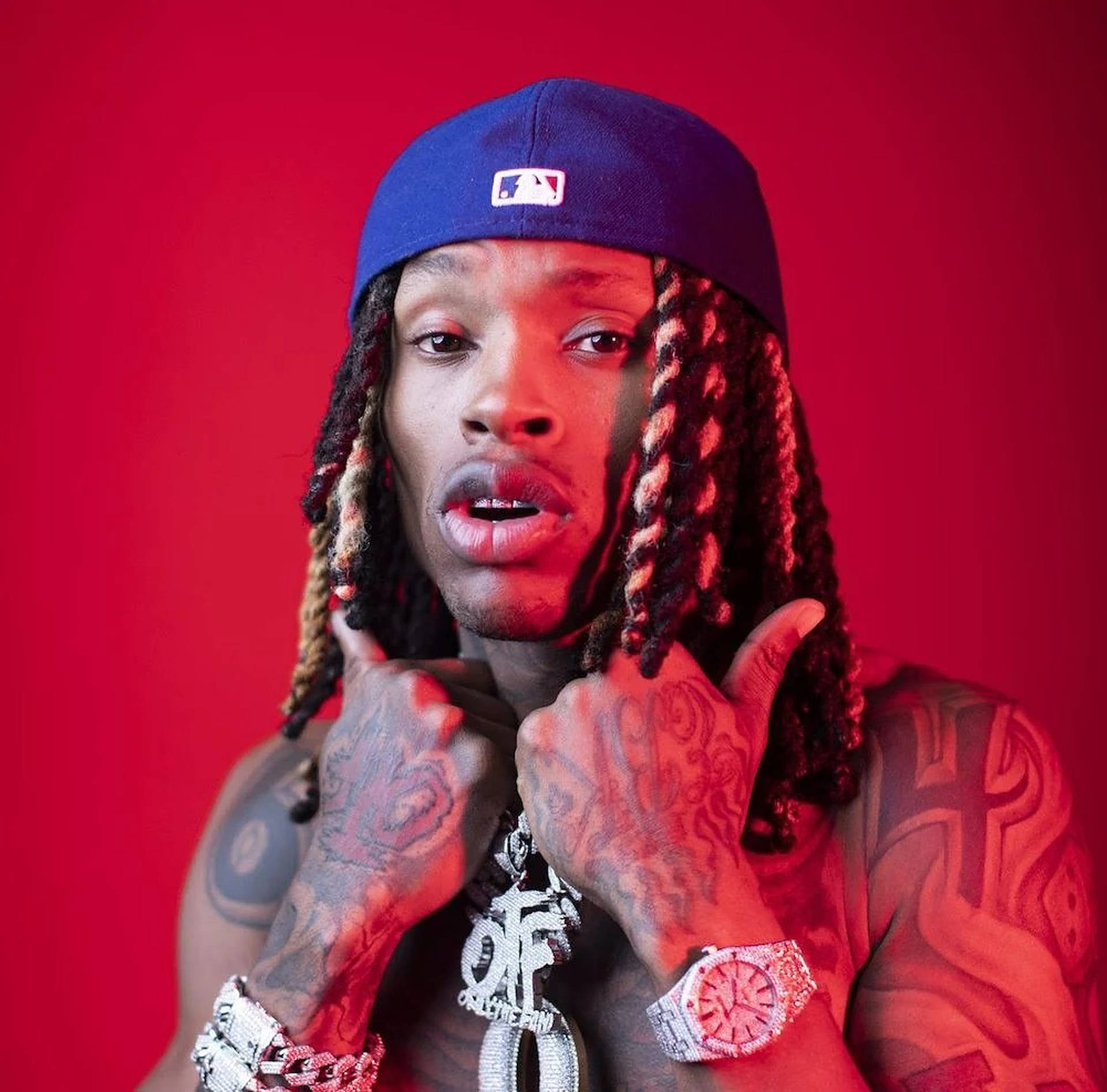 A portrait of a rapper with dreadlocks and tattoos, wearing a baseball cap and jewelry