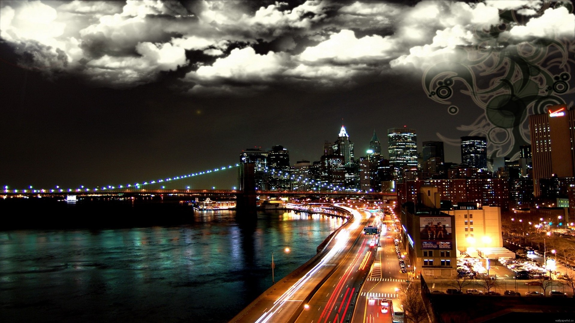 A breathtaking night view of a cityscape with a bridge, a river, and illuminated buildings under a dramatic cloudy sky