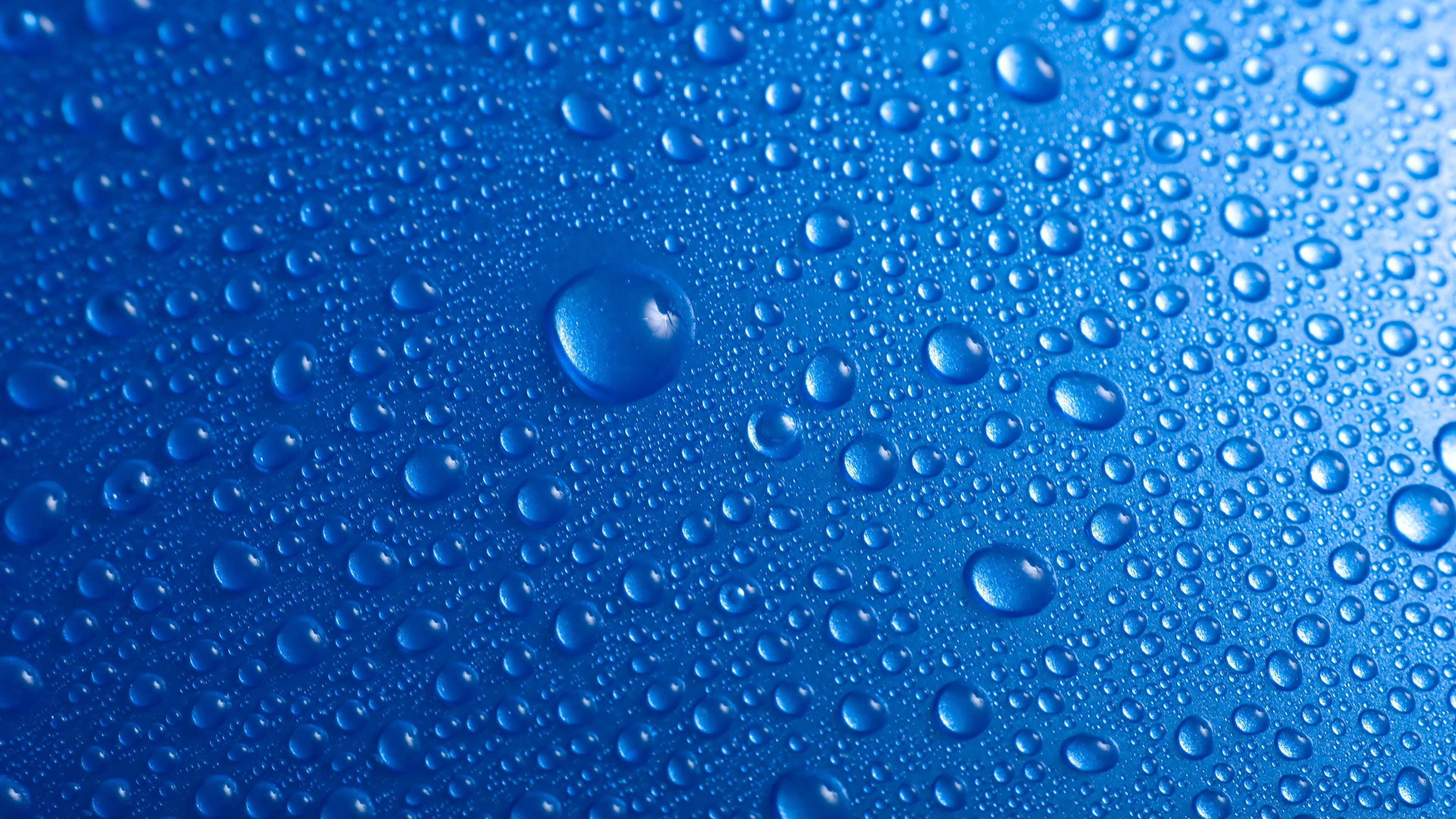 Close-up of water droplets on a vibrant blue surface, creating a textured and refreshing visual
