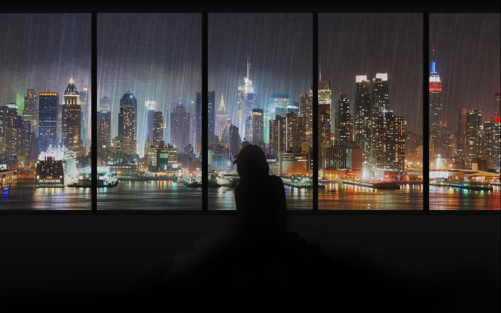 Silhouette of a person looking out a large window at a rainy cityscape at night, evoking a cozy and introspective mood