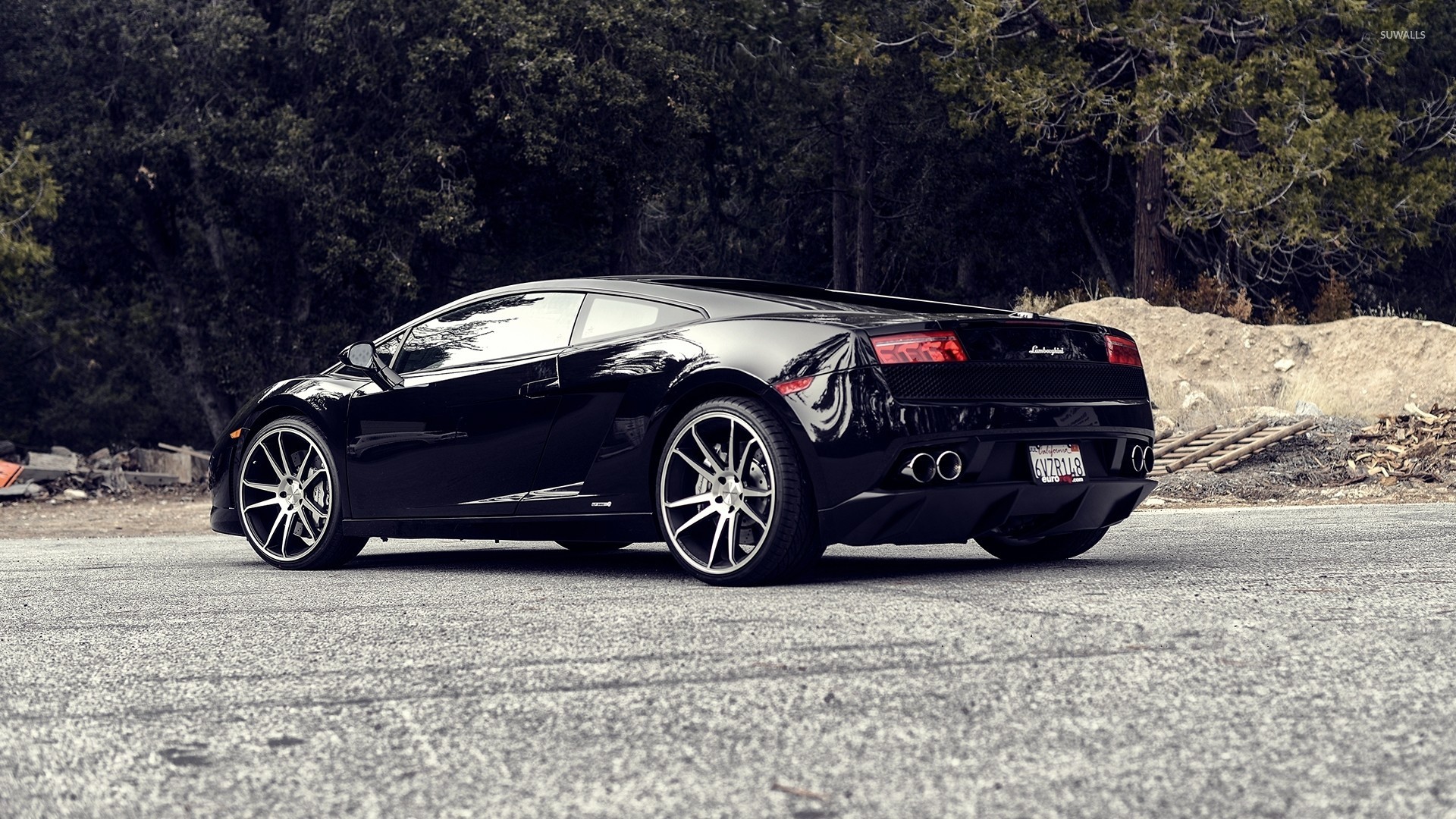 Black Lamborghini Gallardo parked on a paved road near a forested area