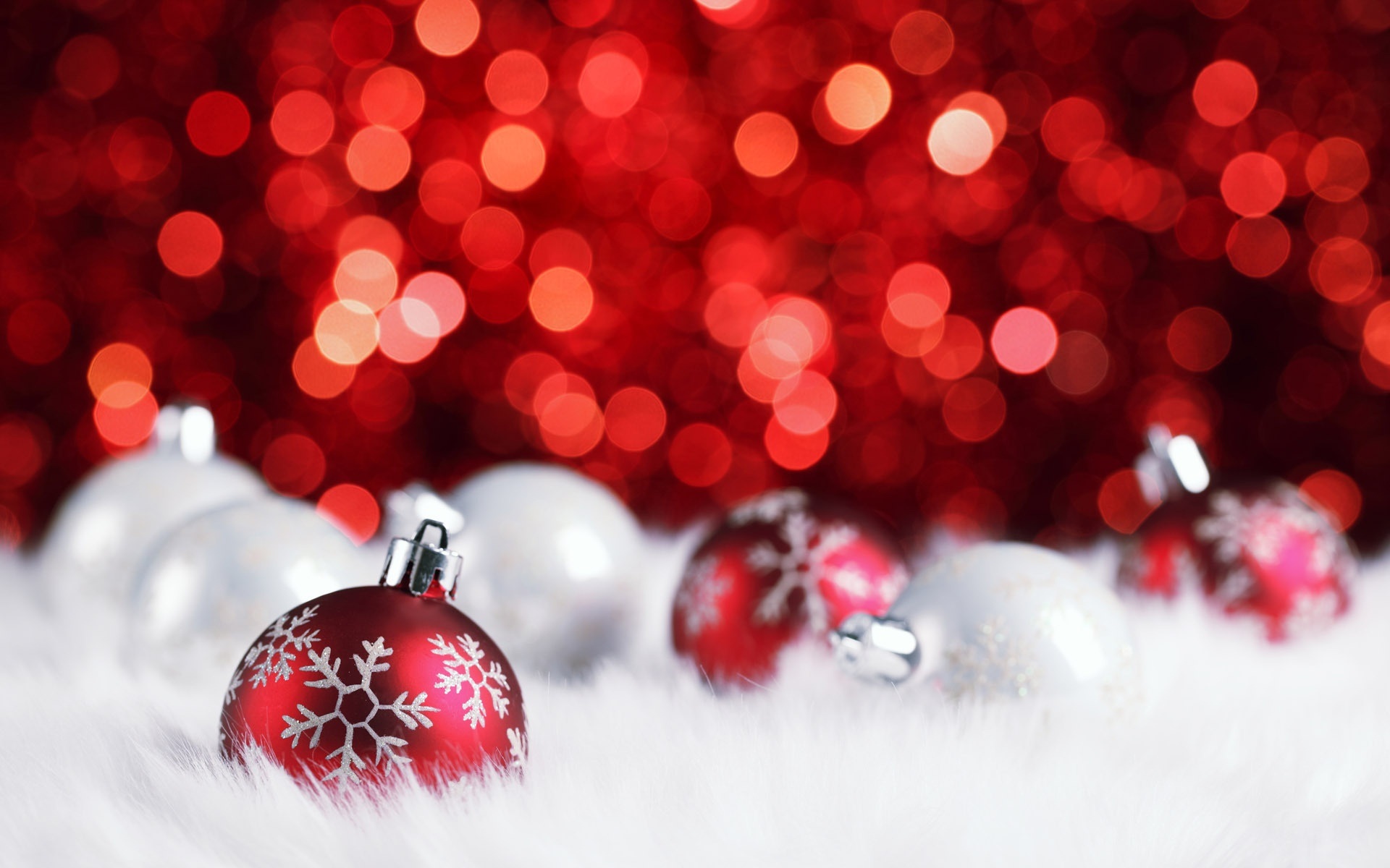 Red and white Christmas ornaments on a white fluffy surface with a red bokeh background