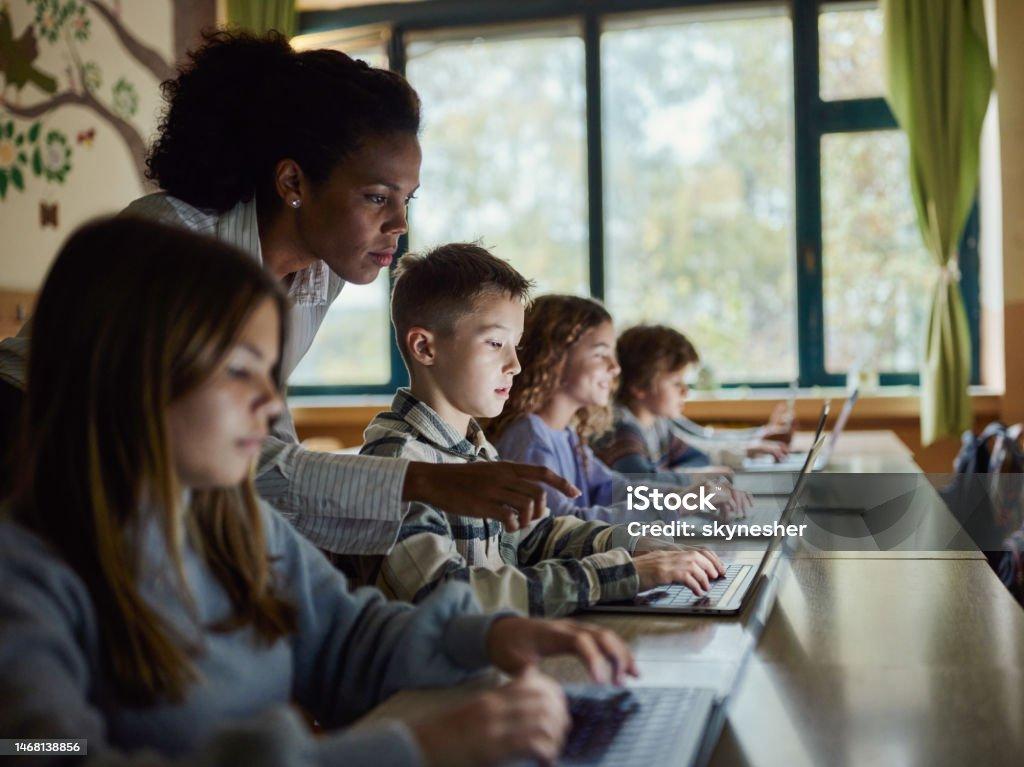 Black Teacher Assisting Students In Using Computers On A Class
