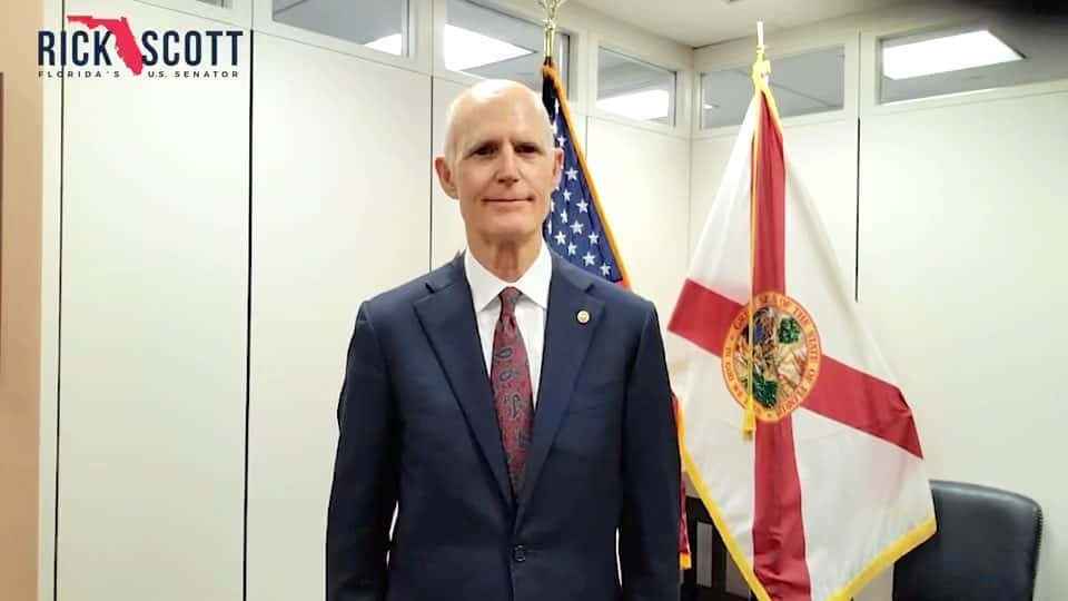 Rick Scott Poses With Flags On Wallpaper