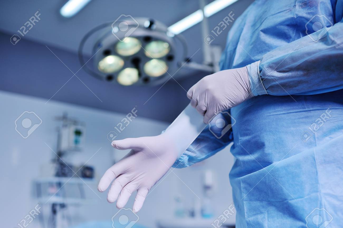 Doctor Puts On Latex Gloves The Background Of Surgical