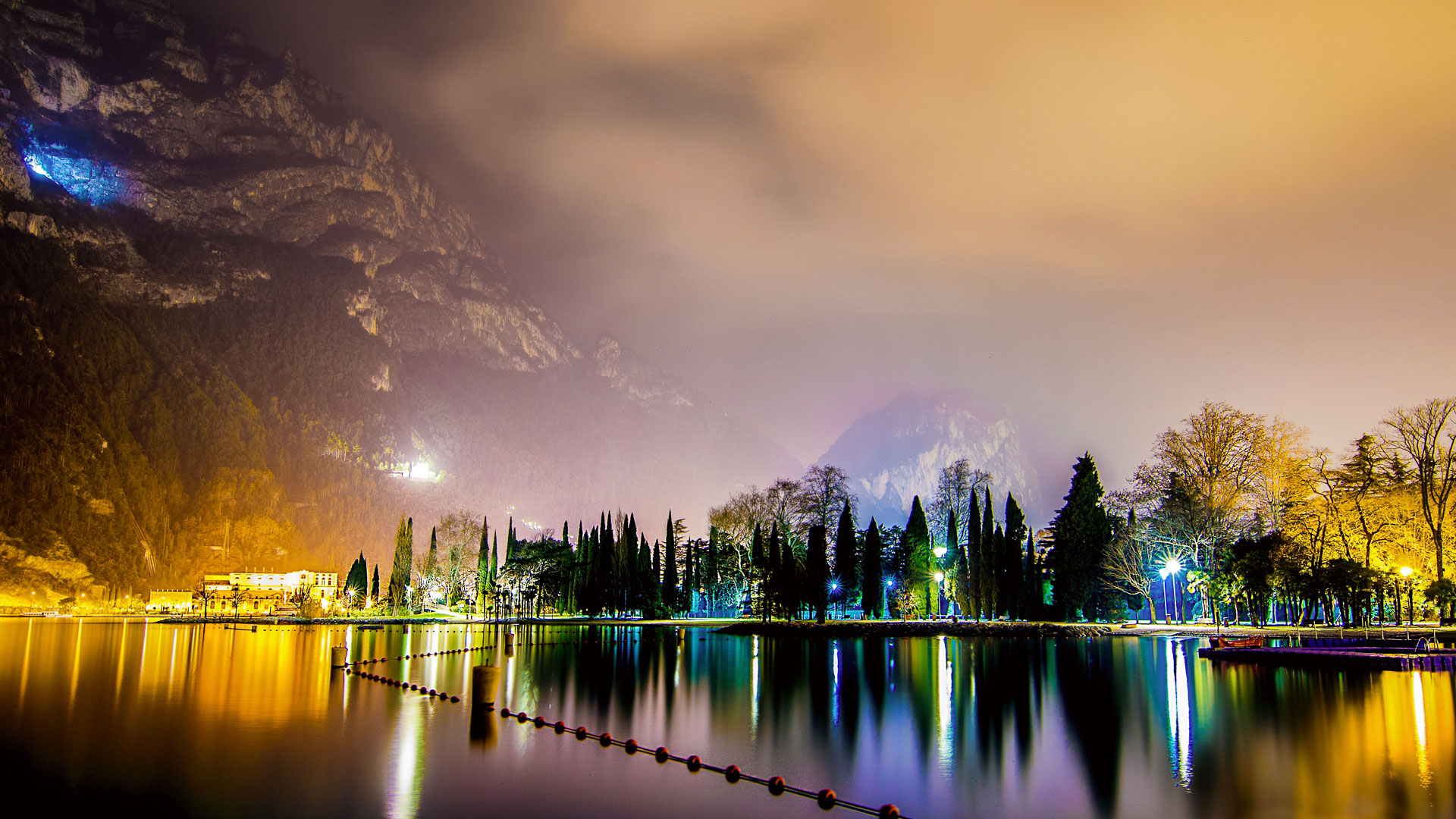 A breathtaking night view of Lake Garda, Italy, with the colorful lights reflecting on the calm water and the mountains in the background