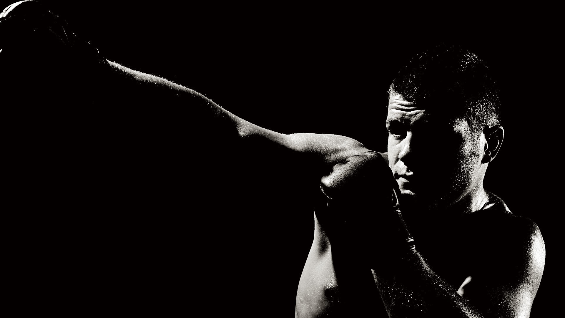 A black and white image of a martial artist throwing a punch in a dark setting, highlighting the intensity and focus of the movement