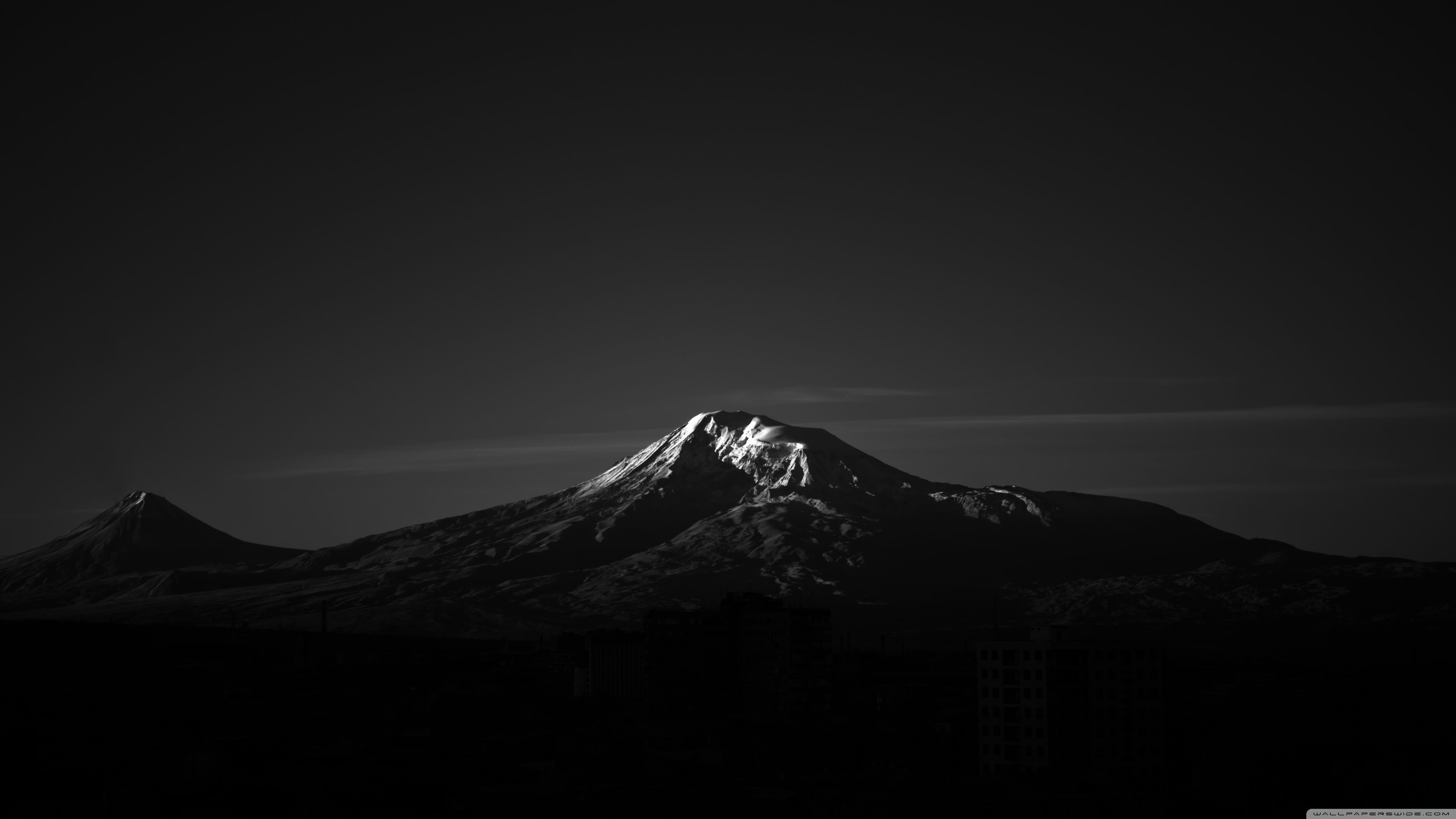 Black and white, minimalist photograph of a snow-capped mountain peak against a dark sky