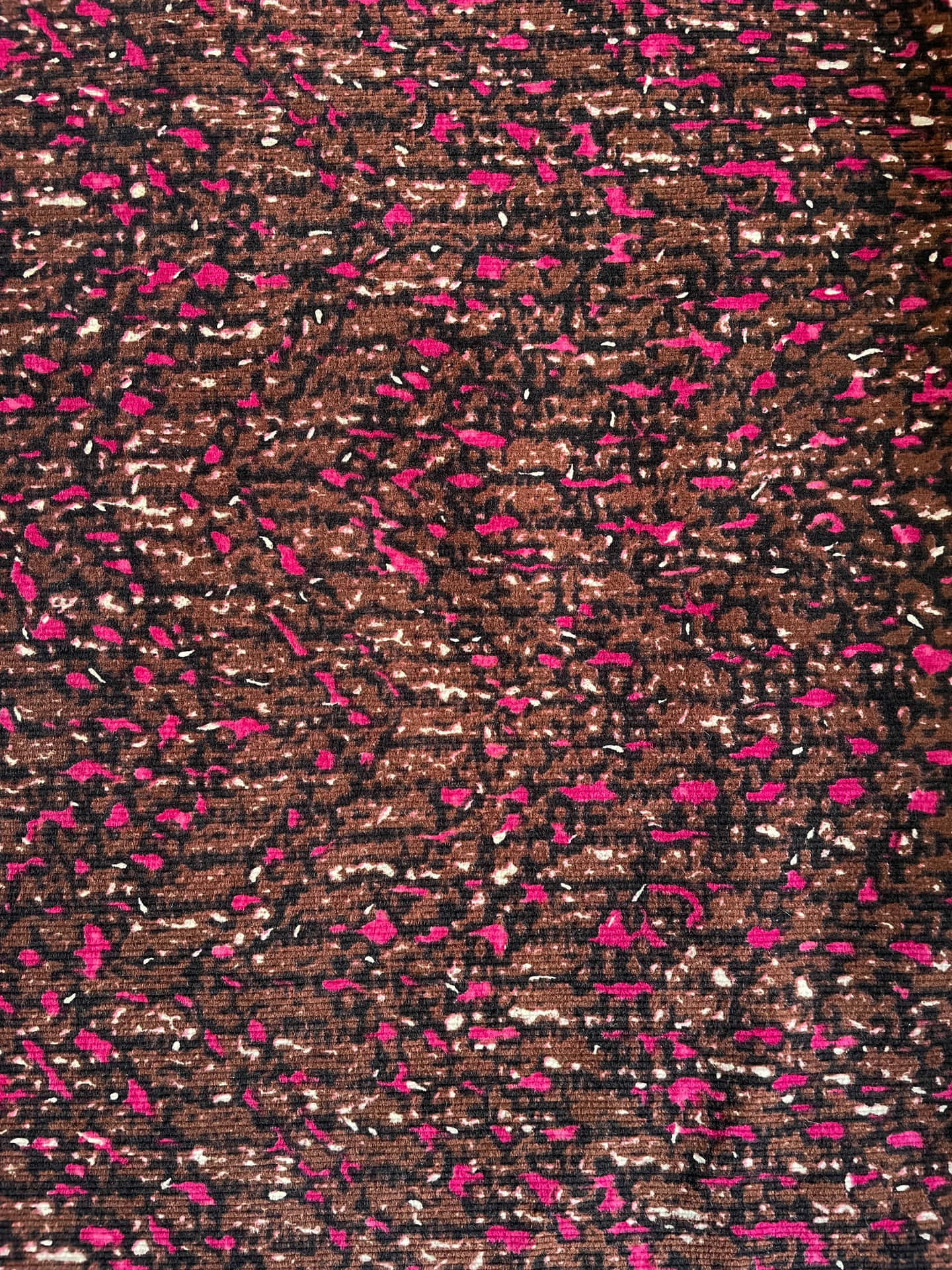 Close-up of a textured fabric with a dark brown background and abstract pink and white specks, resembling a subtle animal print