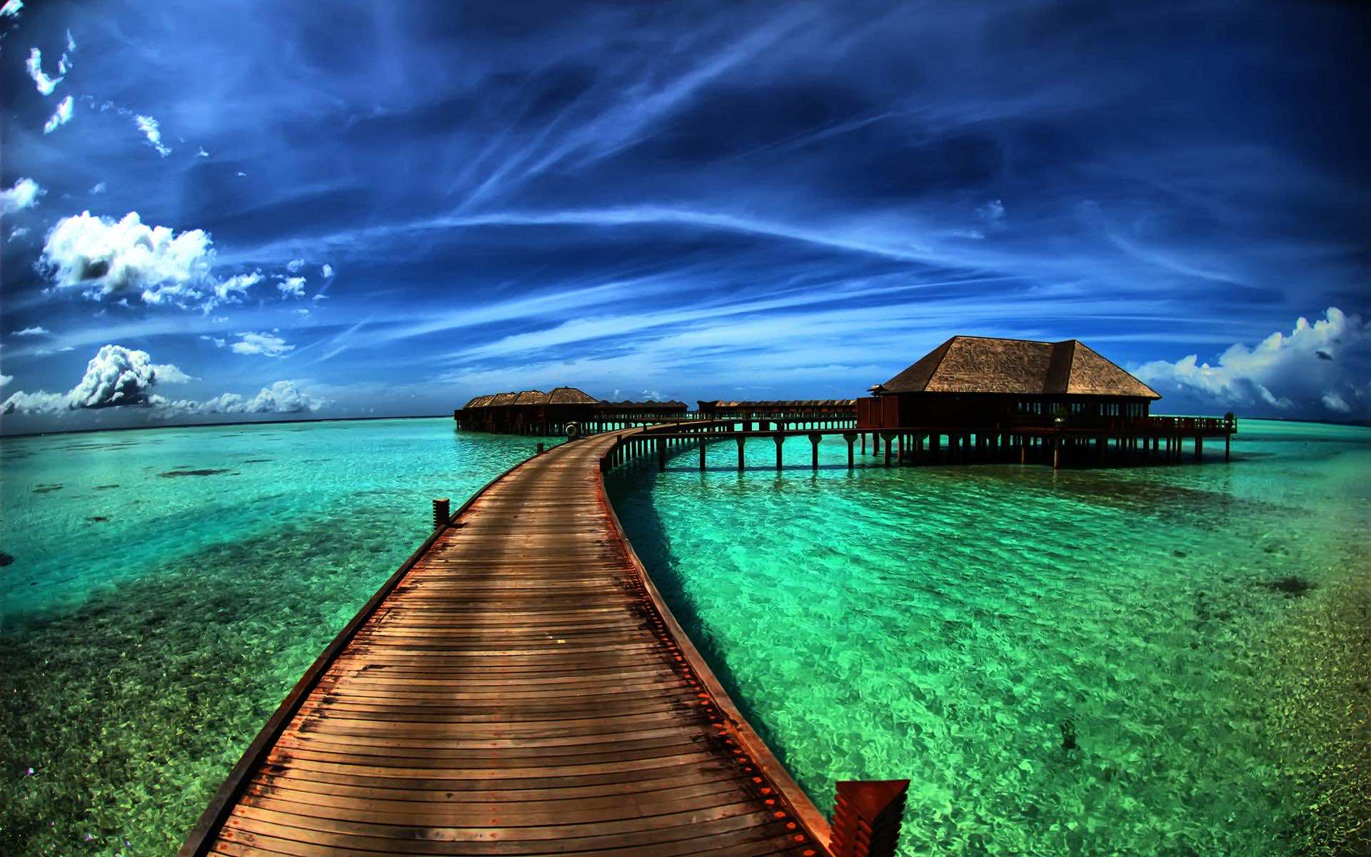 A wooden walkway over turquoise water leading to overwater bungalows in the Maldives