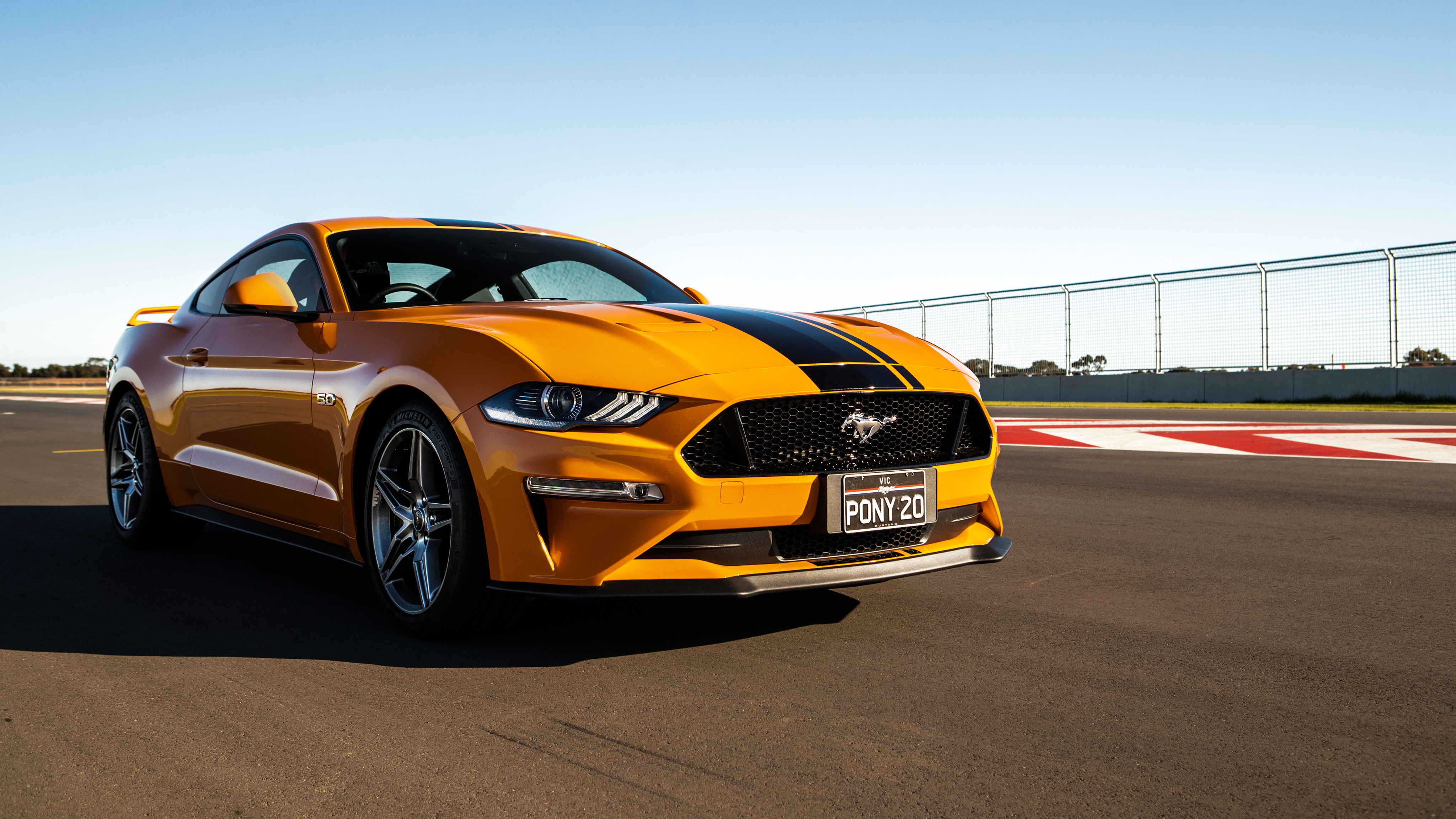 A vibrant orange Ford Mustang with black racing stripes parked on a race track