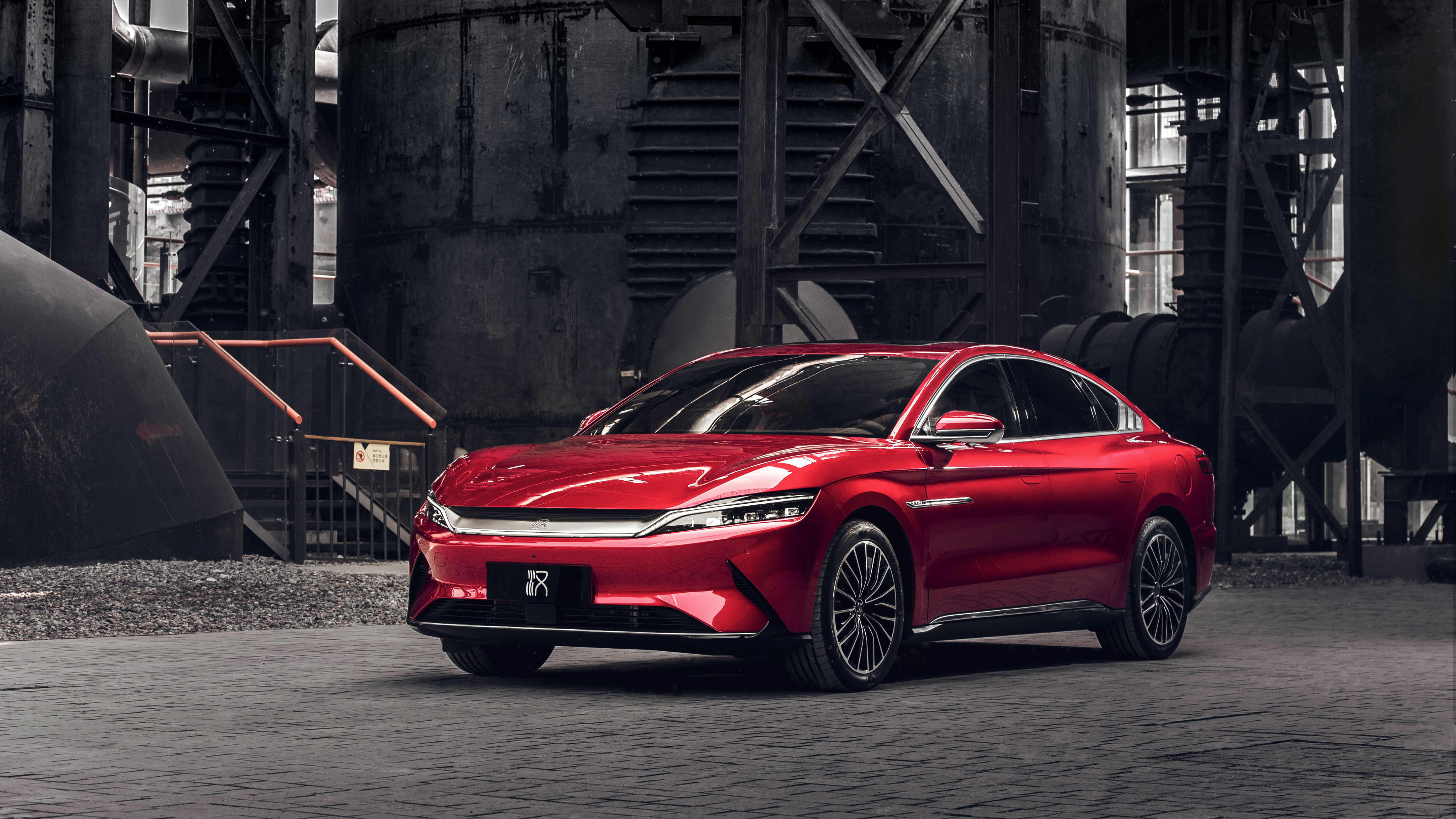 A vibrant red BYD Seal electric sedan parked in an industrial setting, highlighting its sleek design and modern features