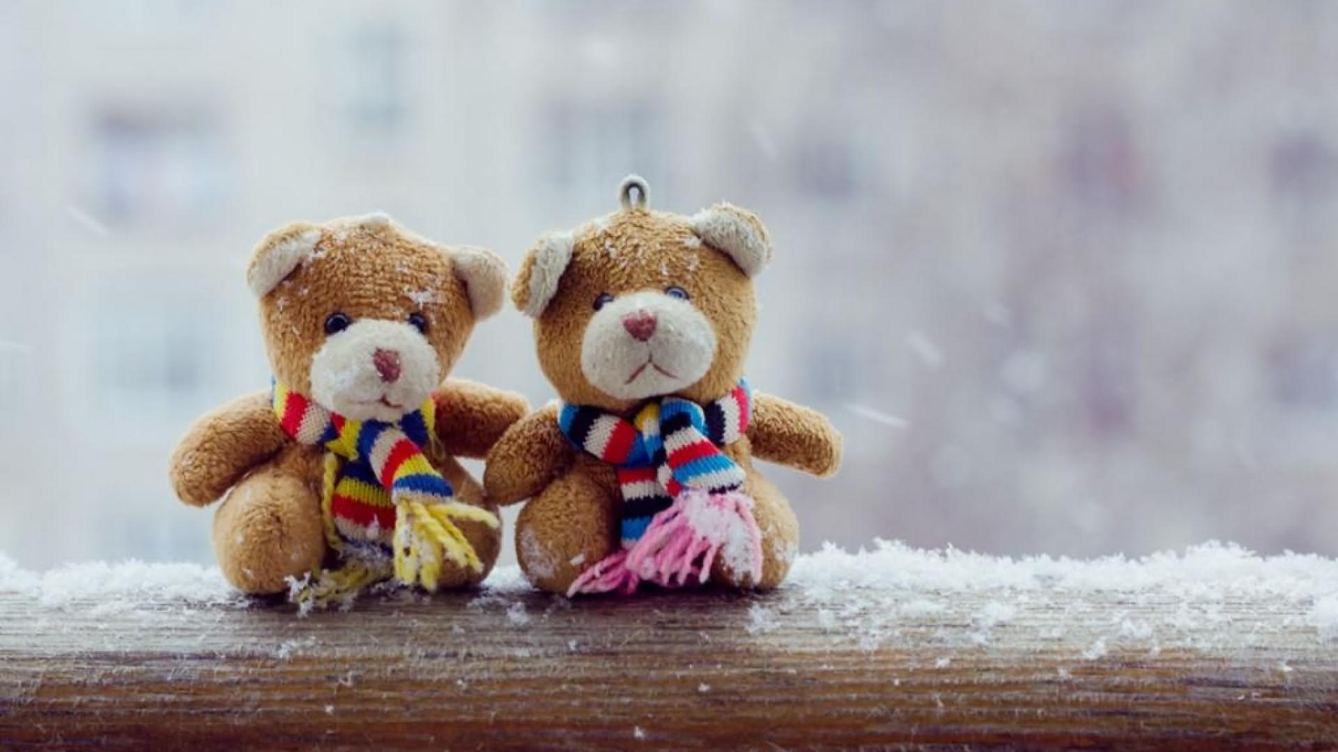 Two teddy bears wearing scarves sit on snow covered wooden surface, symbolizing friendship and warmth during winter