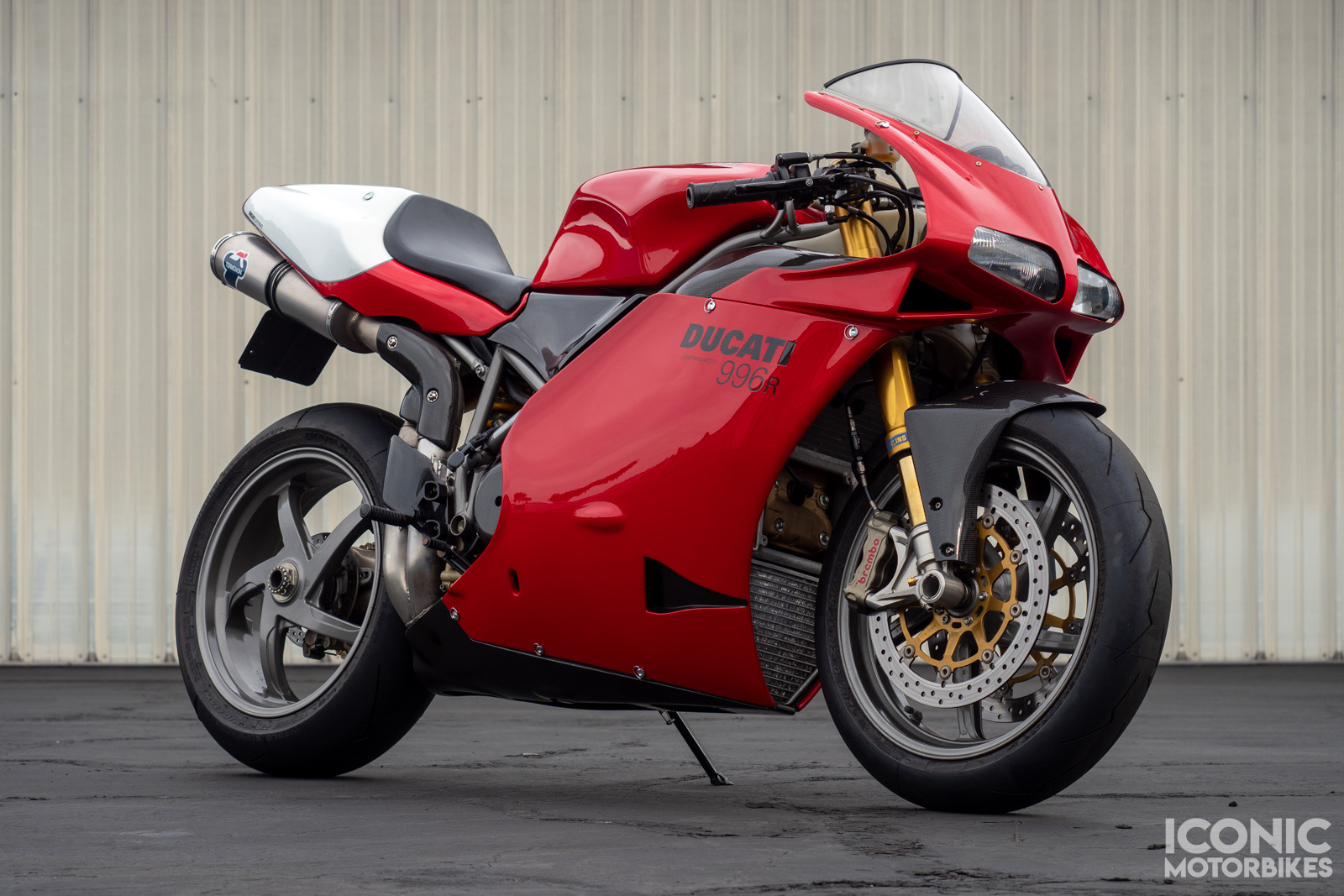 A Ducati 996 sportbike in red and white, parked in front of a corrugated metal wall