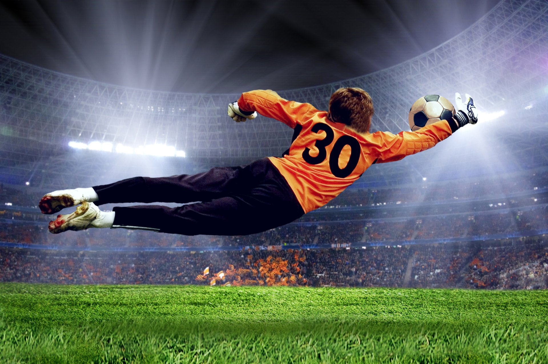 A soccer goalie dives to catch the ball mid-air in a packed stadium