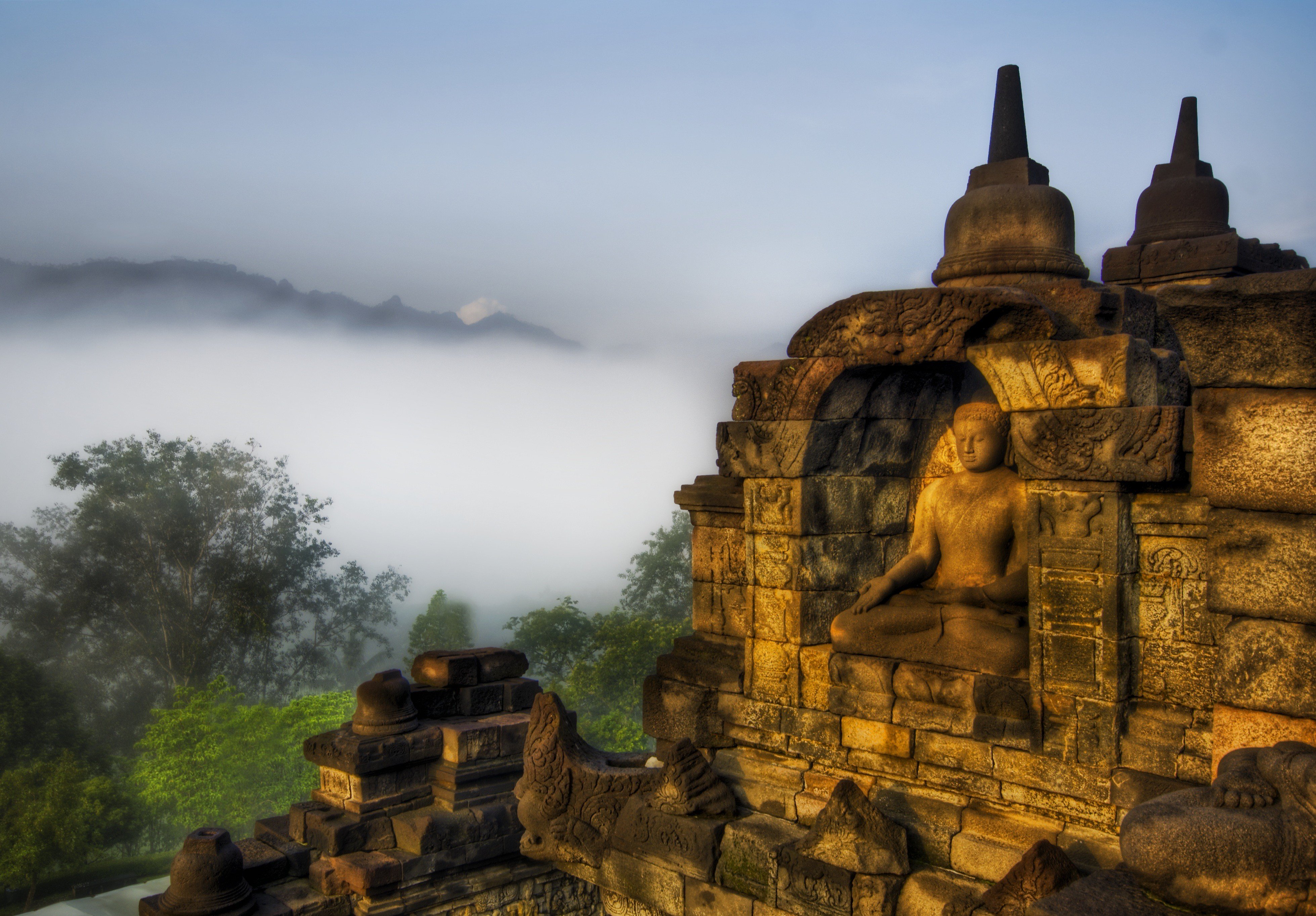 Serene Buddha statue in a stone niche at Borobudur Temple, Indonesia, with misty mountains in the background