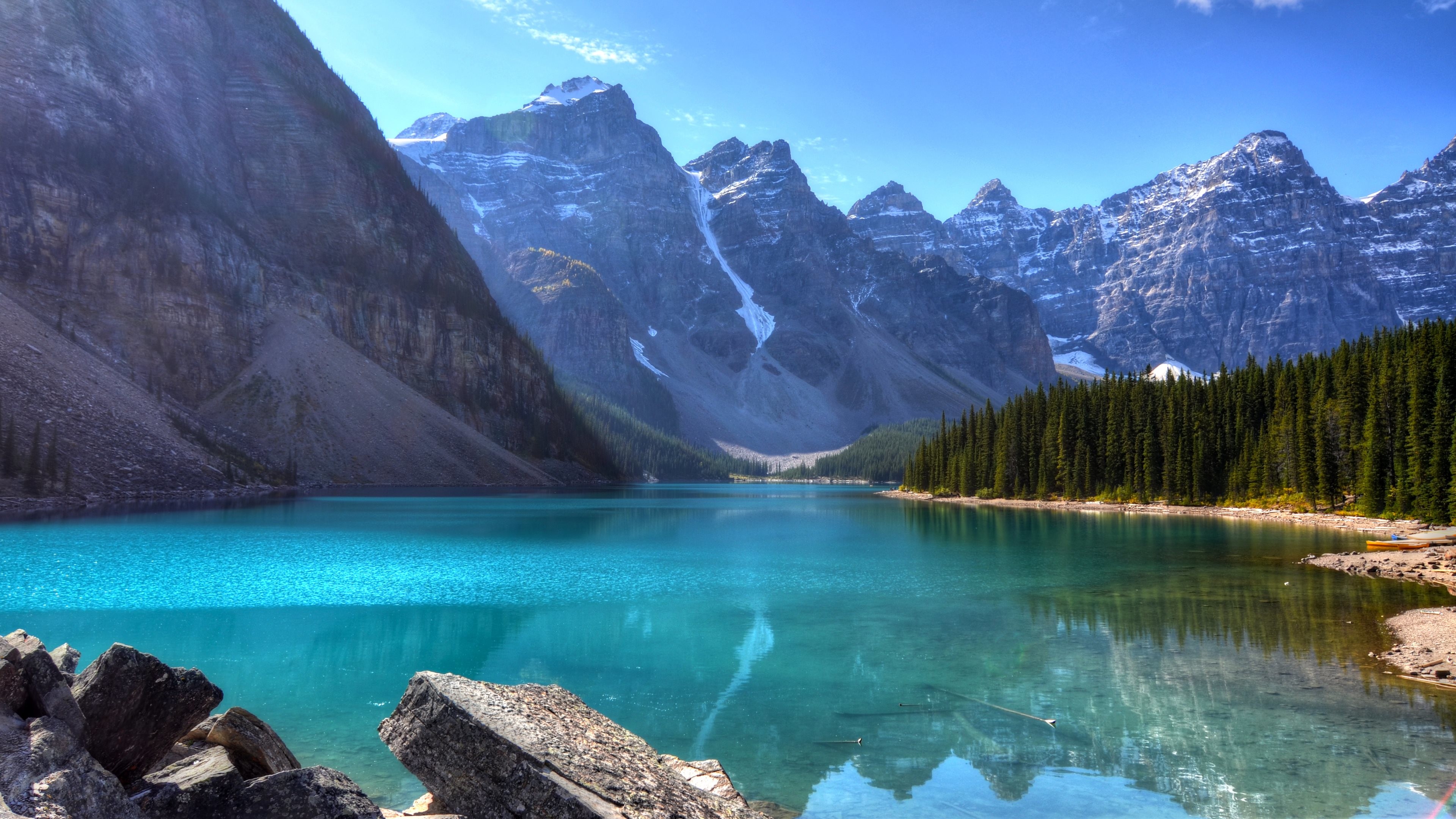 Stunning 4k wallpaper of a turquoise lake nestled amidst snow-capped mountains and a pine forest