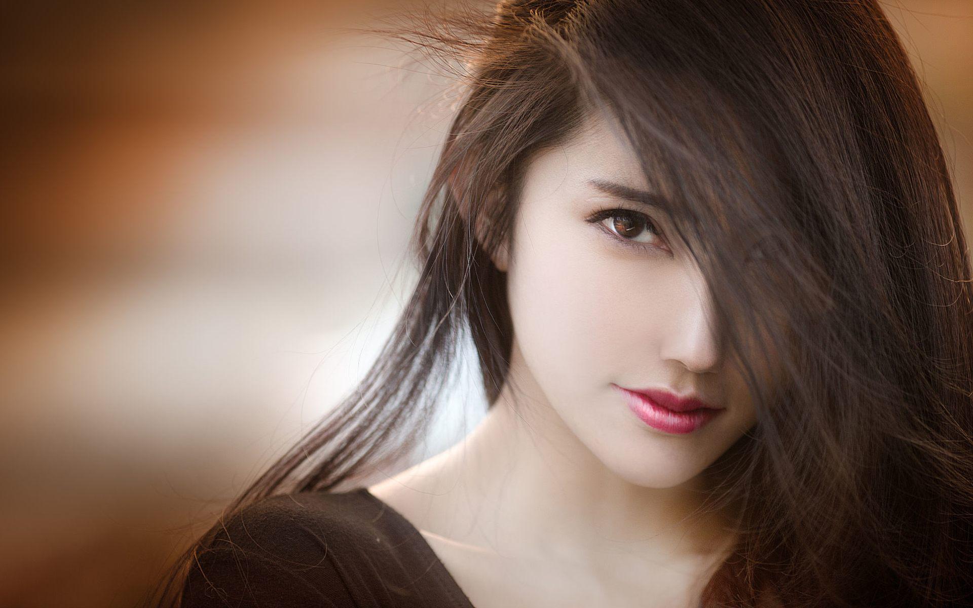 Close-up portrait of a young woman with long, dark hair partially covering her face, creating a mysterious and alluring look