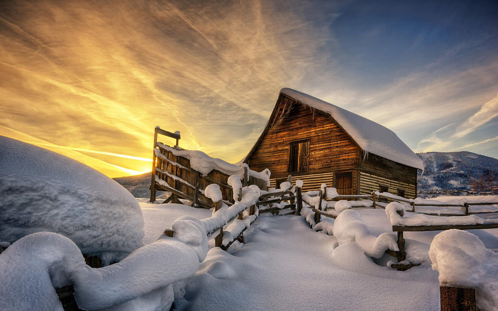 A rustic wooden barn stands in a snow-covered field at sunset, creating a picturesque winter scene