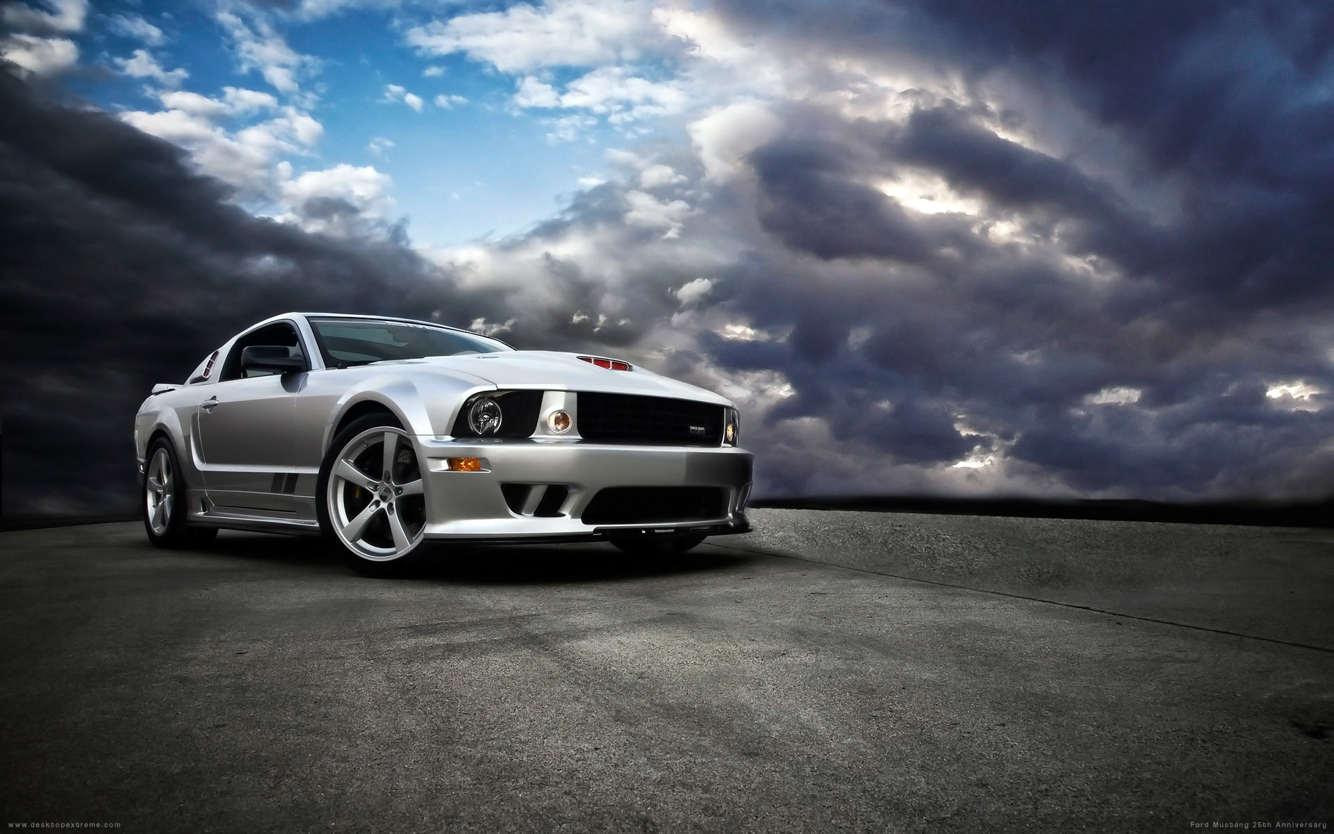 A silver Ford Mustang Saleen S281 Extreme parked on a paved surface under a dramatic cloudy sky