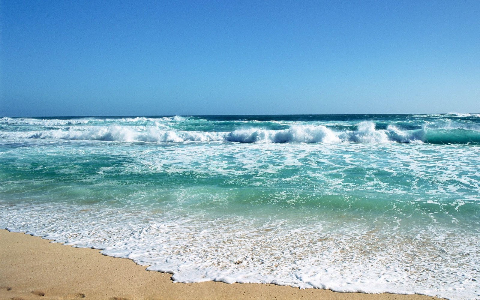 Turquoise ocean waves crashing on a sandy beach under a clear blue sky