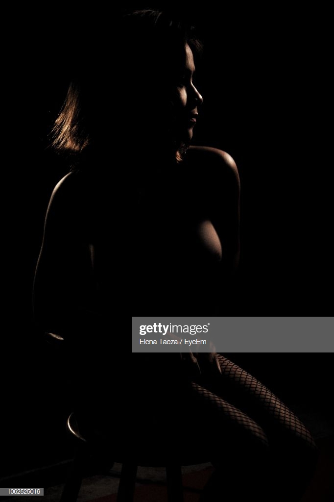 Seductive Young Woman Sitting Against Black Background Stock Photo