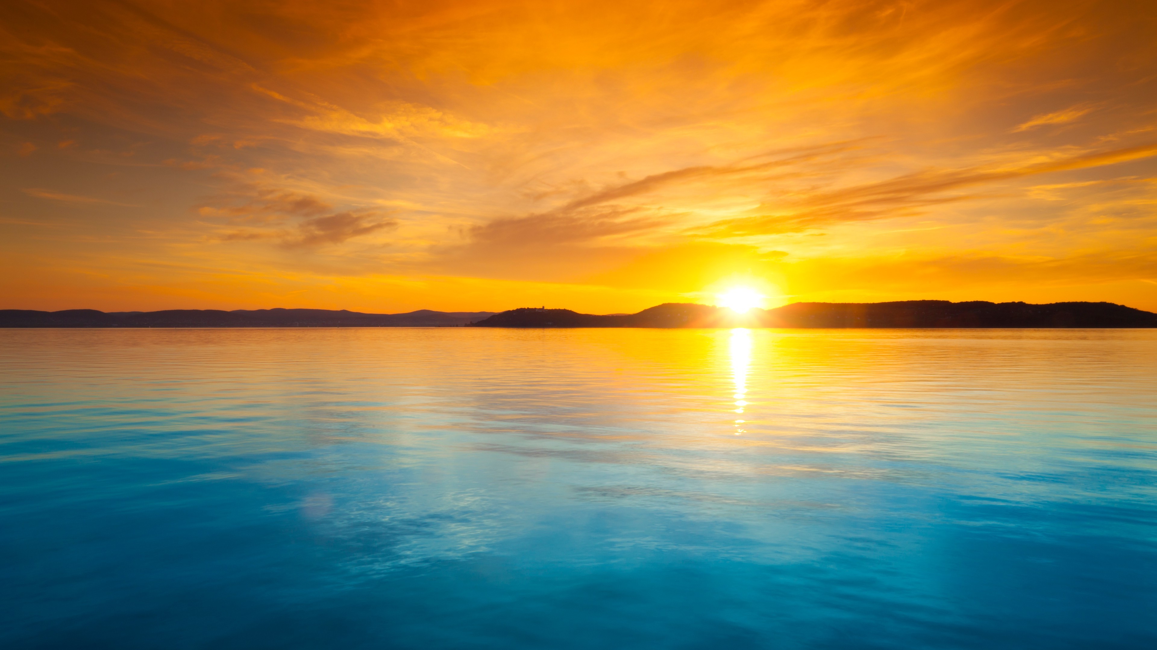 A breathtaking sunset over a tranquil body of water, with the sun casting a warm golden glow across the sky and reflecting on the calm surface