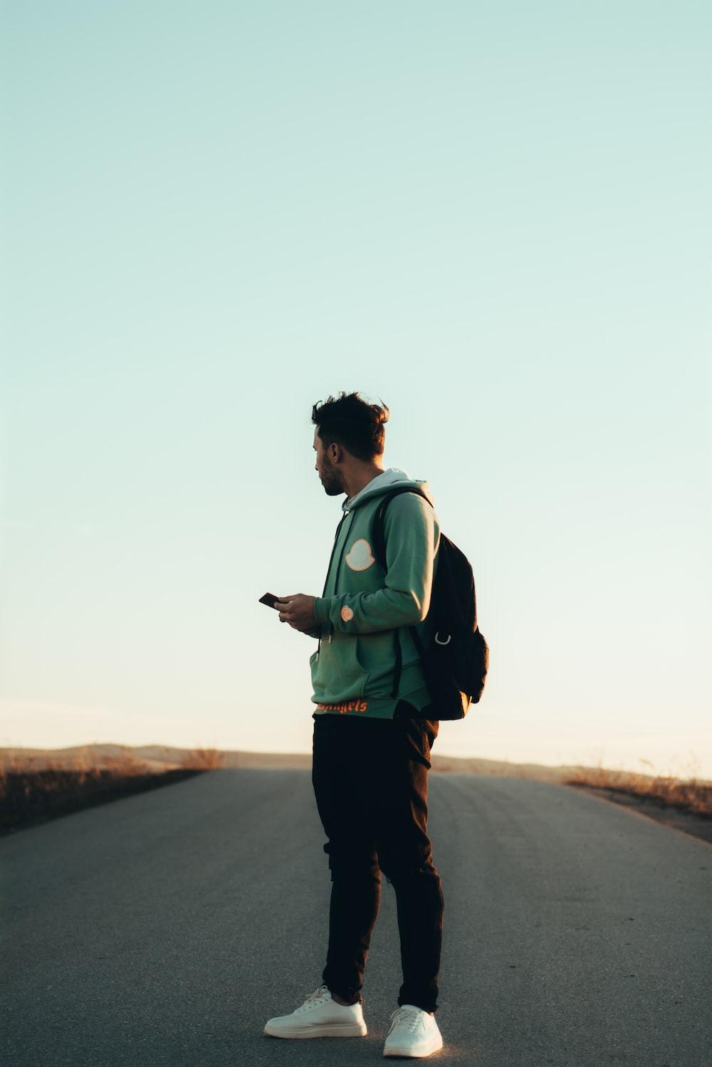 Man In Green Jacket And Black Pants Standing On Road During