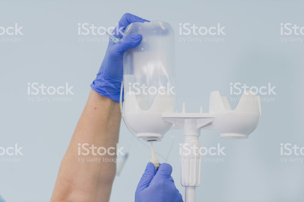 Doctors Hand And Infusion Drip In Hospital On Blurred Background