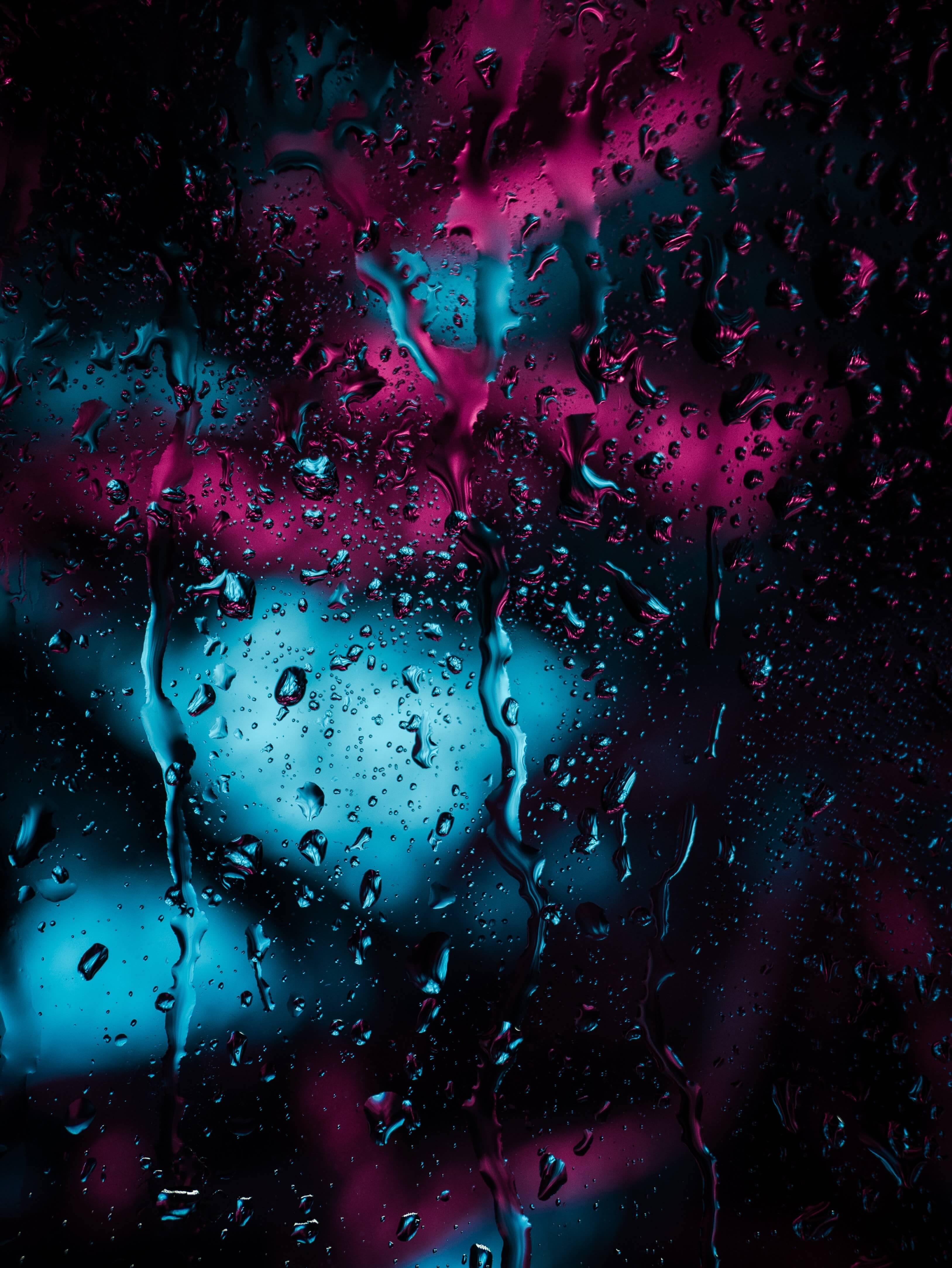 Close-up of raindrops on a window pane, illuminated by vibrant neon lights in teal and magenta, creating a cyberpunk-inspired abstract image