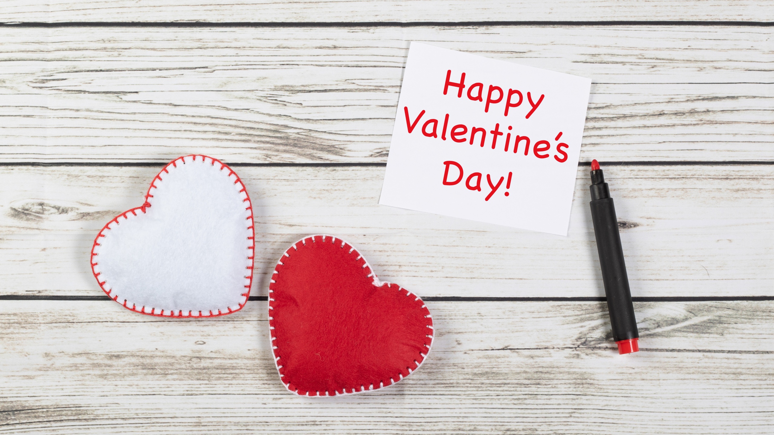 Two felt hearts and a 'Happy Valentine's Day' note on a white wooden background