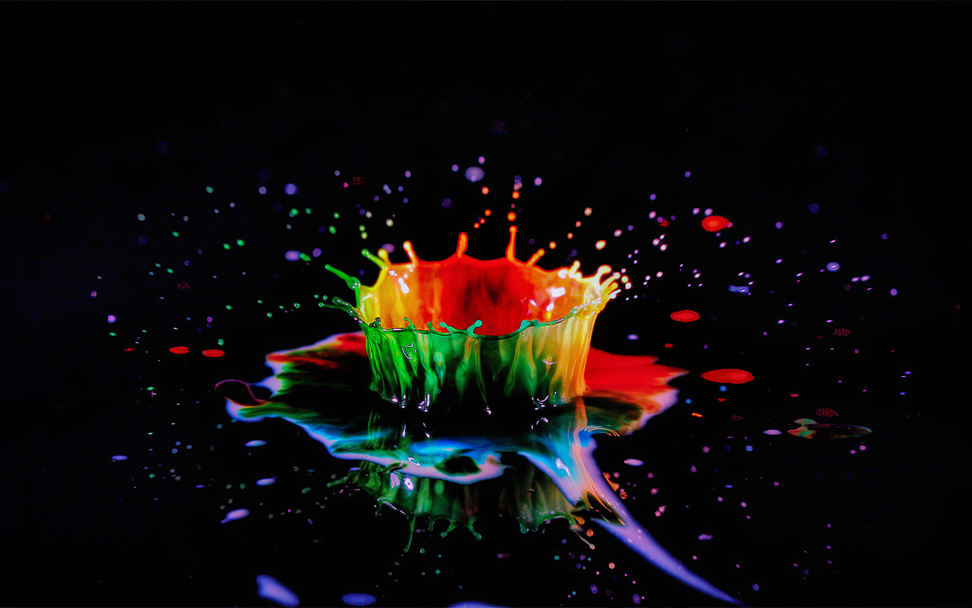 A vibrant splash of colorful water erupts against a black background, creating a stunning crown-like formation with droplets scattering around. Perfect for a water-themed wallpaper