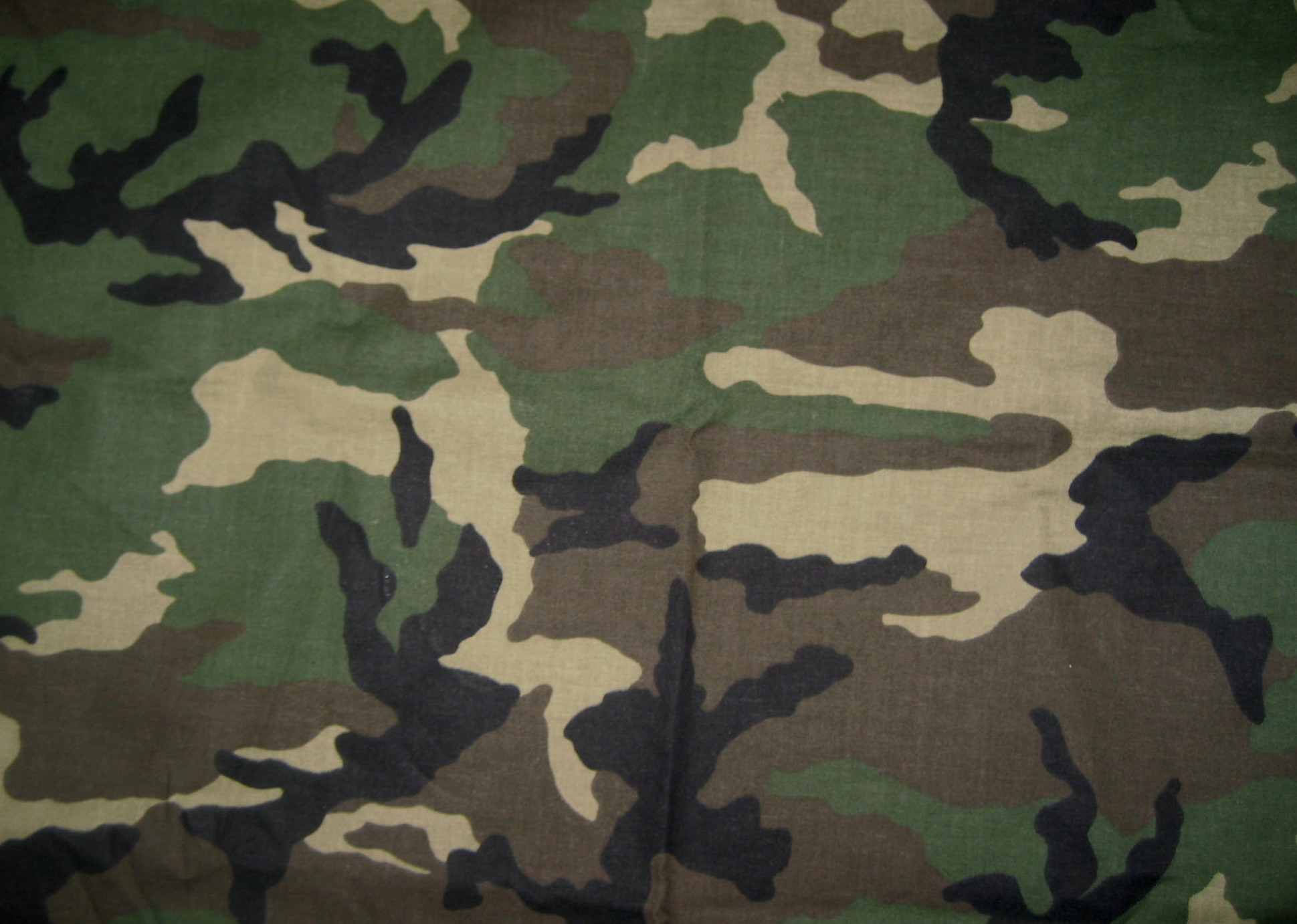 Close-up of woodland camouflage fabric, showcasing its irregular pattern of green, brown, and black shapes designed for concealment in natural environments
