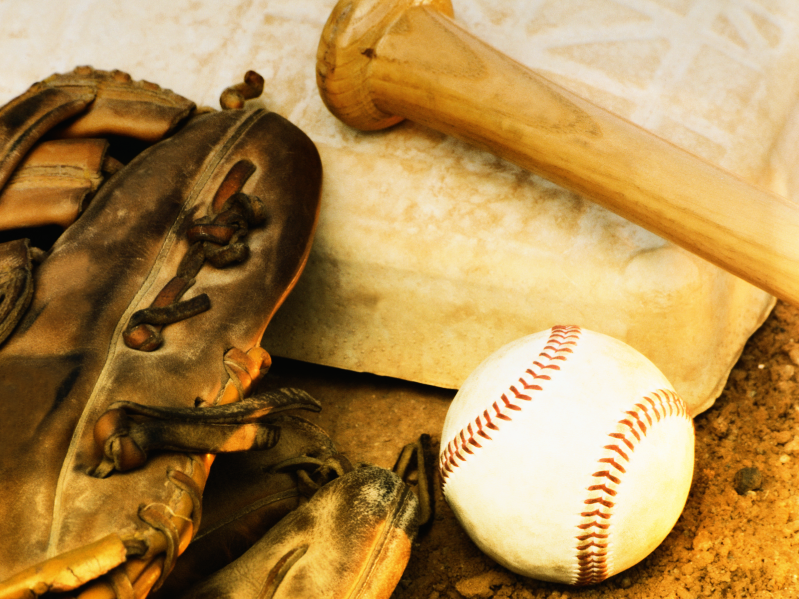 Close-up of baseball equipment: worn leather glove, wooden bat, and baseball on dirt field