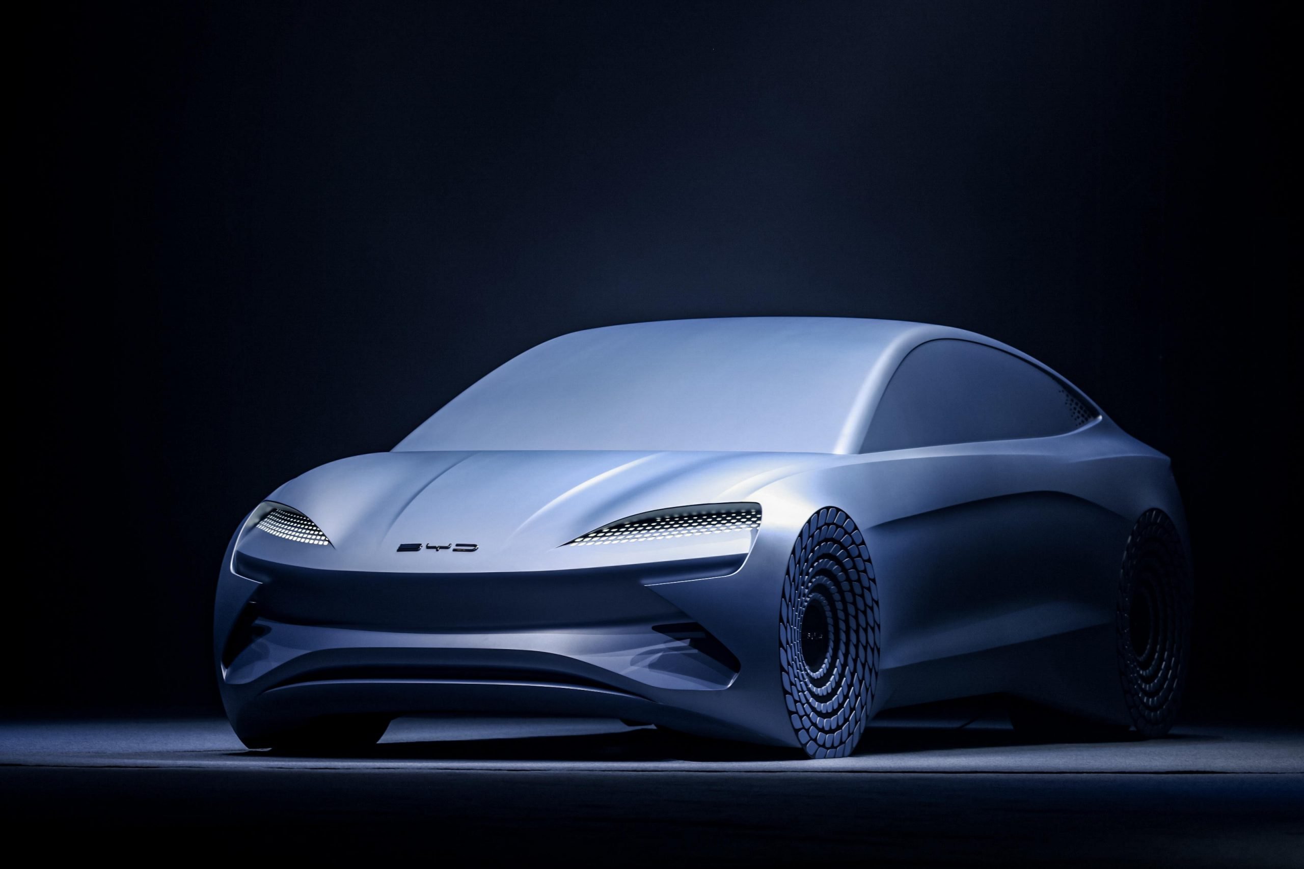 A futuristic BYD Shark concept car, rendered in a sleek, silver-gray finish, against a dark background. The car's innovative wheel design and smooth body lines are prominently displayed