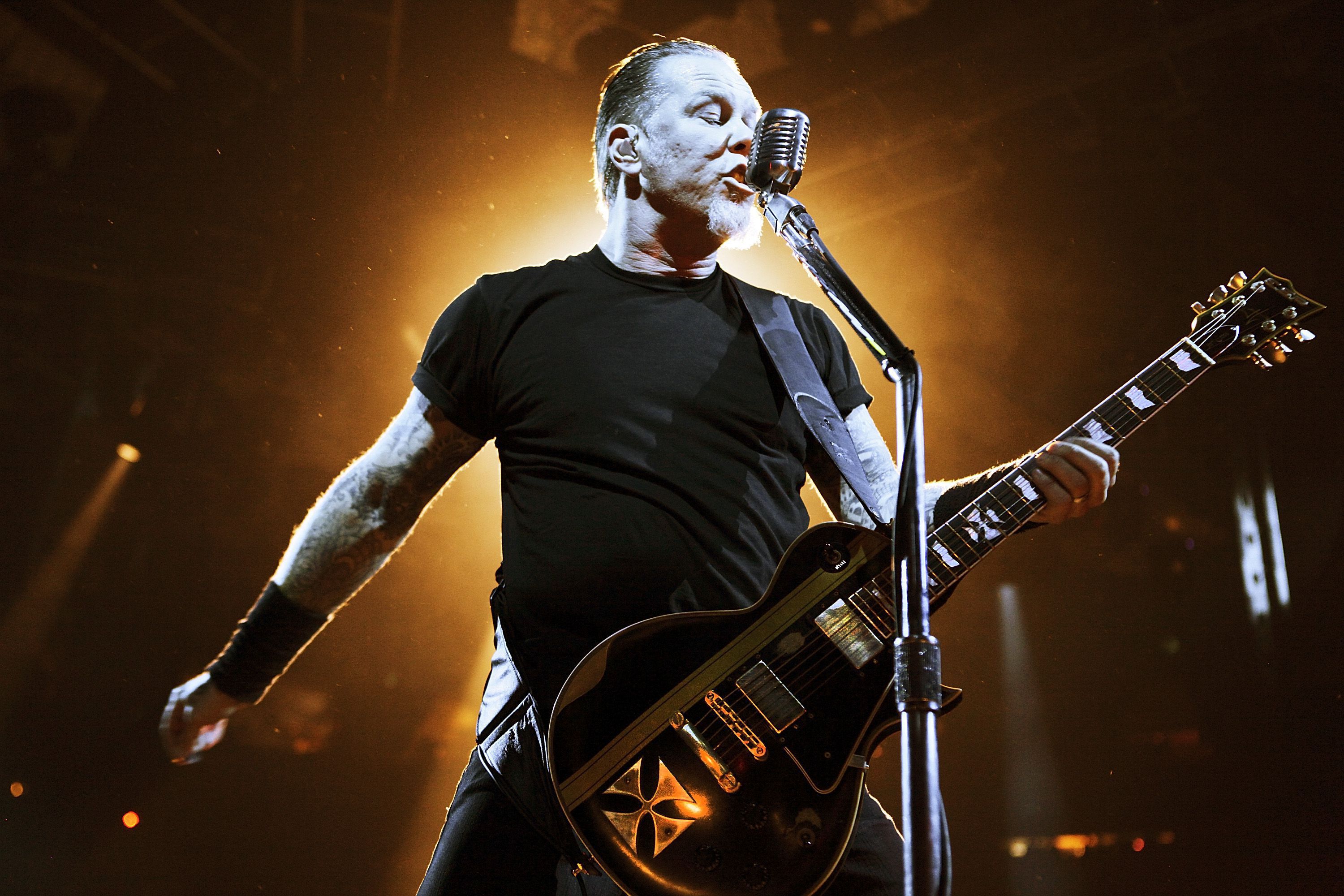 James Hetfield of Metallica performing live on stage, wielding his signature Explorer guitar and singing into a microphone