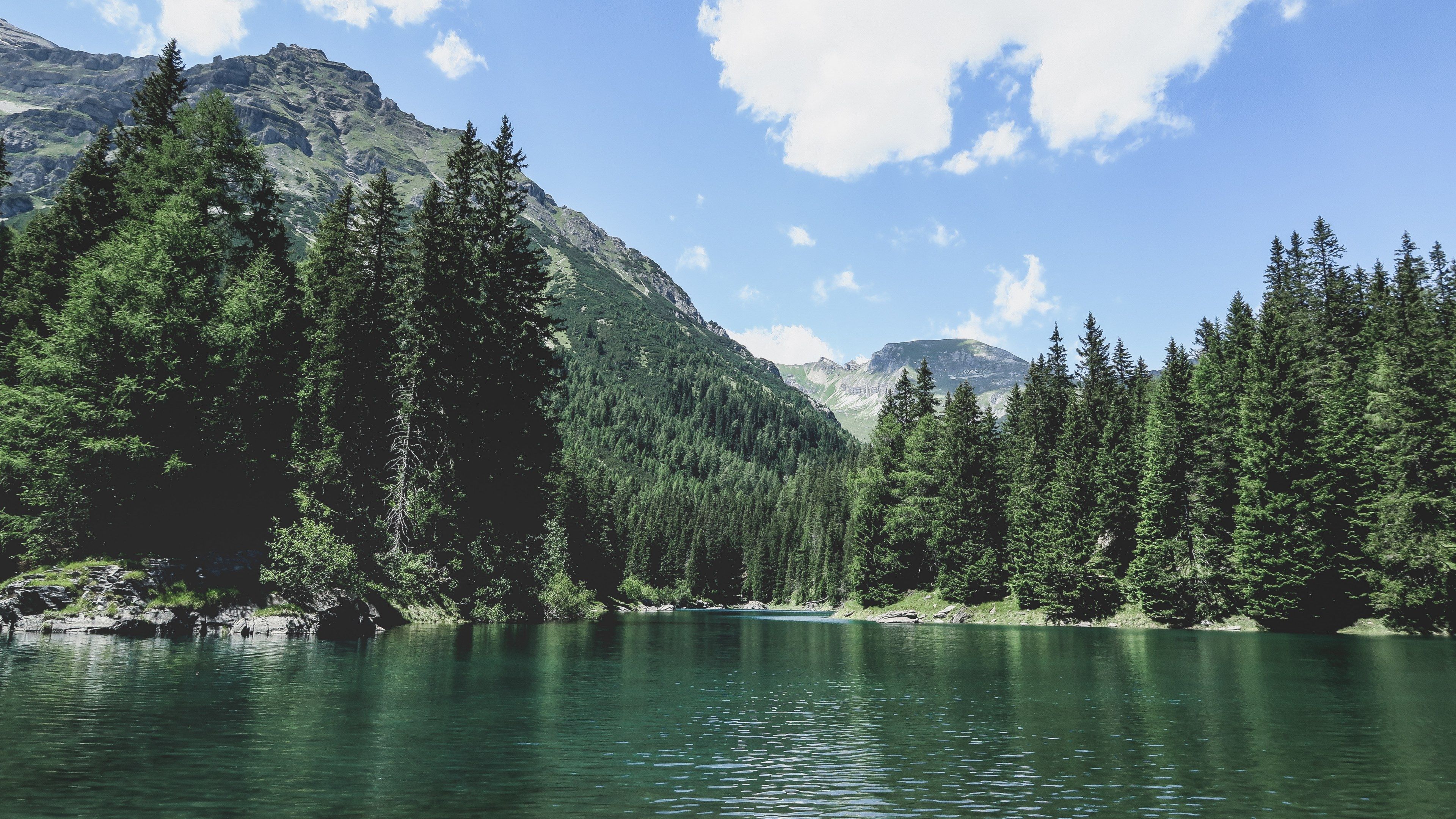 Serene alpine lake nestled amidst lush evergreen forests and majestic mountains under a vibrant blue sky