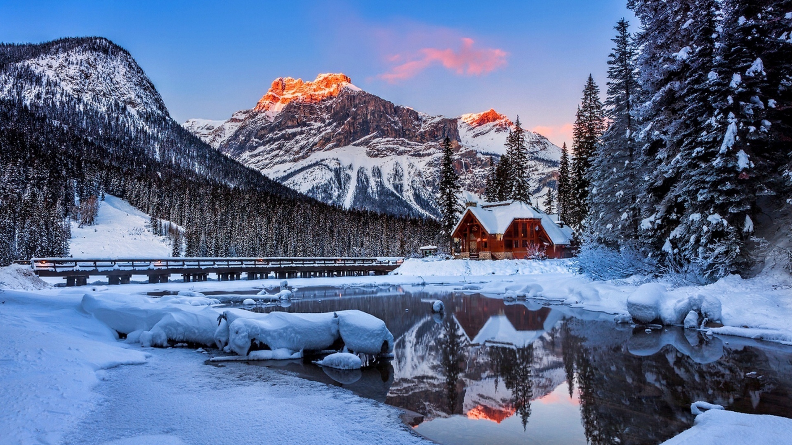 A breathtaking winter landscape with snow-covered mountains, a frozen lake reflecting the warm hues of sunrise, a cozy wooden cabin, and snow-dusted pine trees