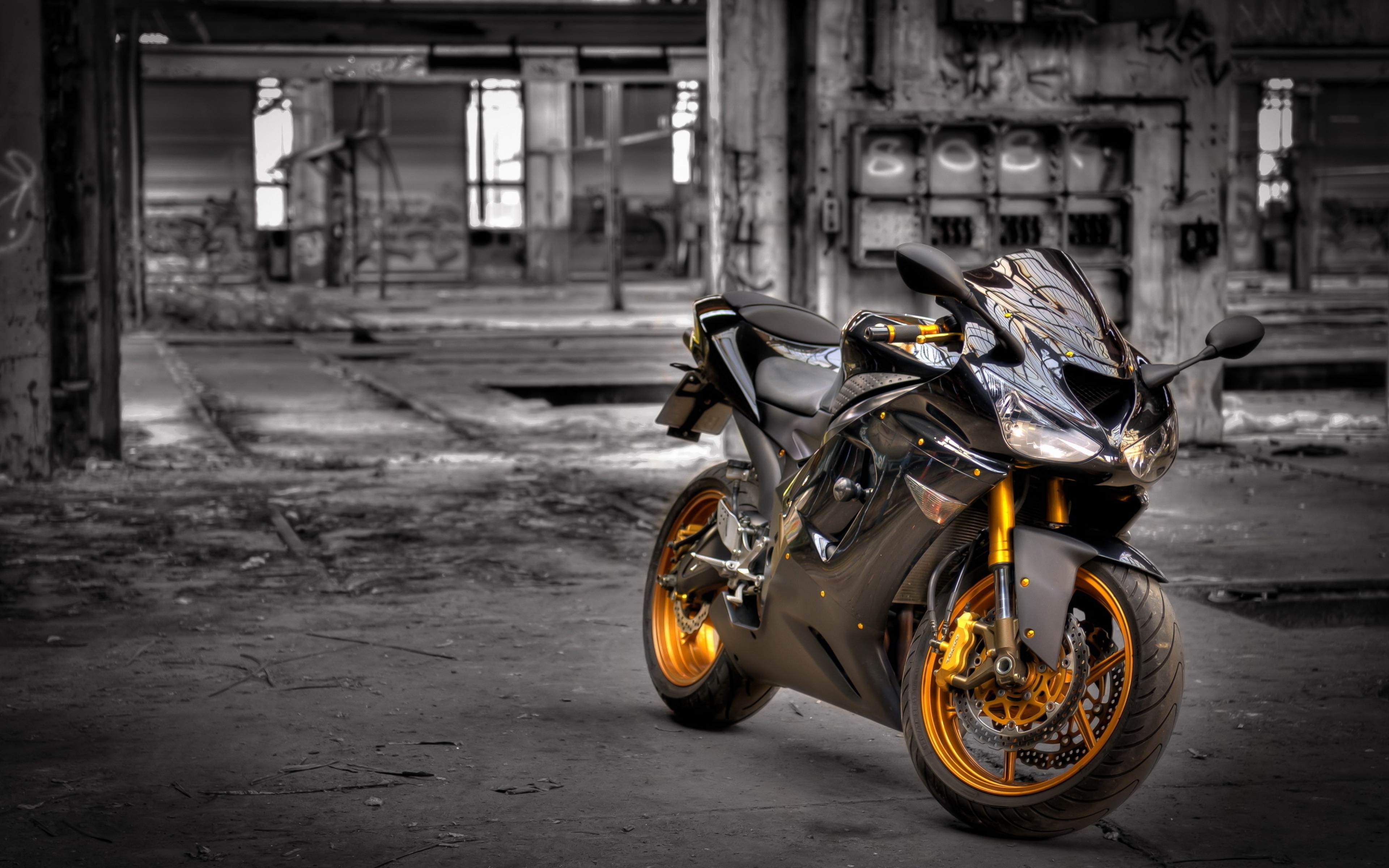 A sleek black sports motorcycle with gold rims parked in an abandoned industrial setting. The contrast between the bike and the gritty background creates a visually striking image