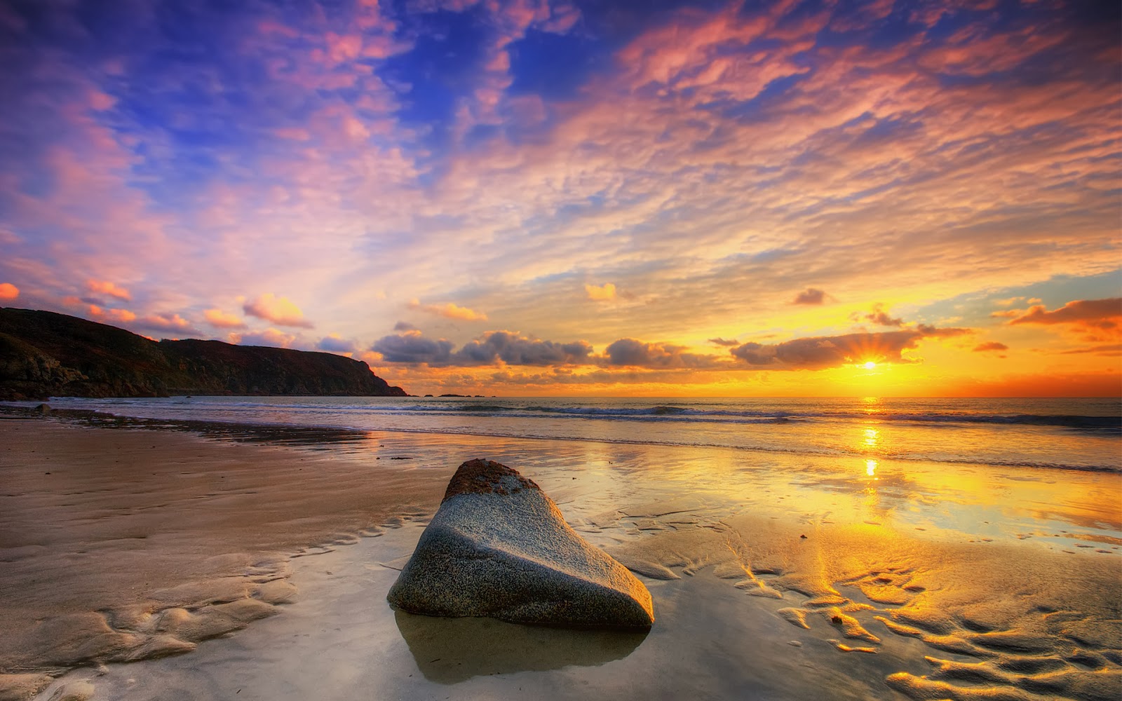 A breathtaking sunset over a tranquil beach, with the golden light reflecting on the wet sand and a prominent rock in the foreground