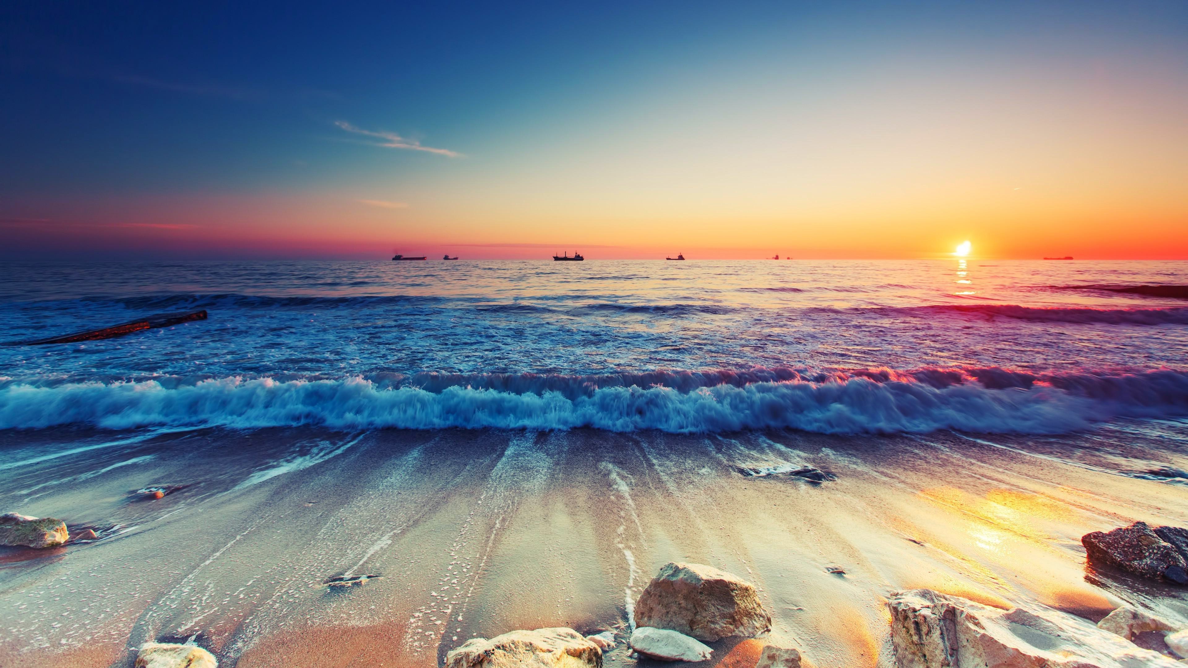 A breathtaking sunset over a vibrant ocean, with gentle waves washing onto a sandy beach dotted with rocks