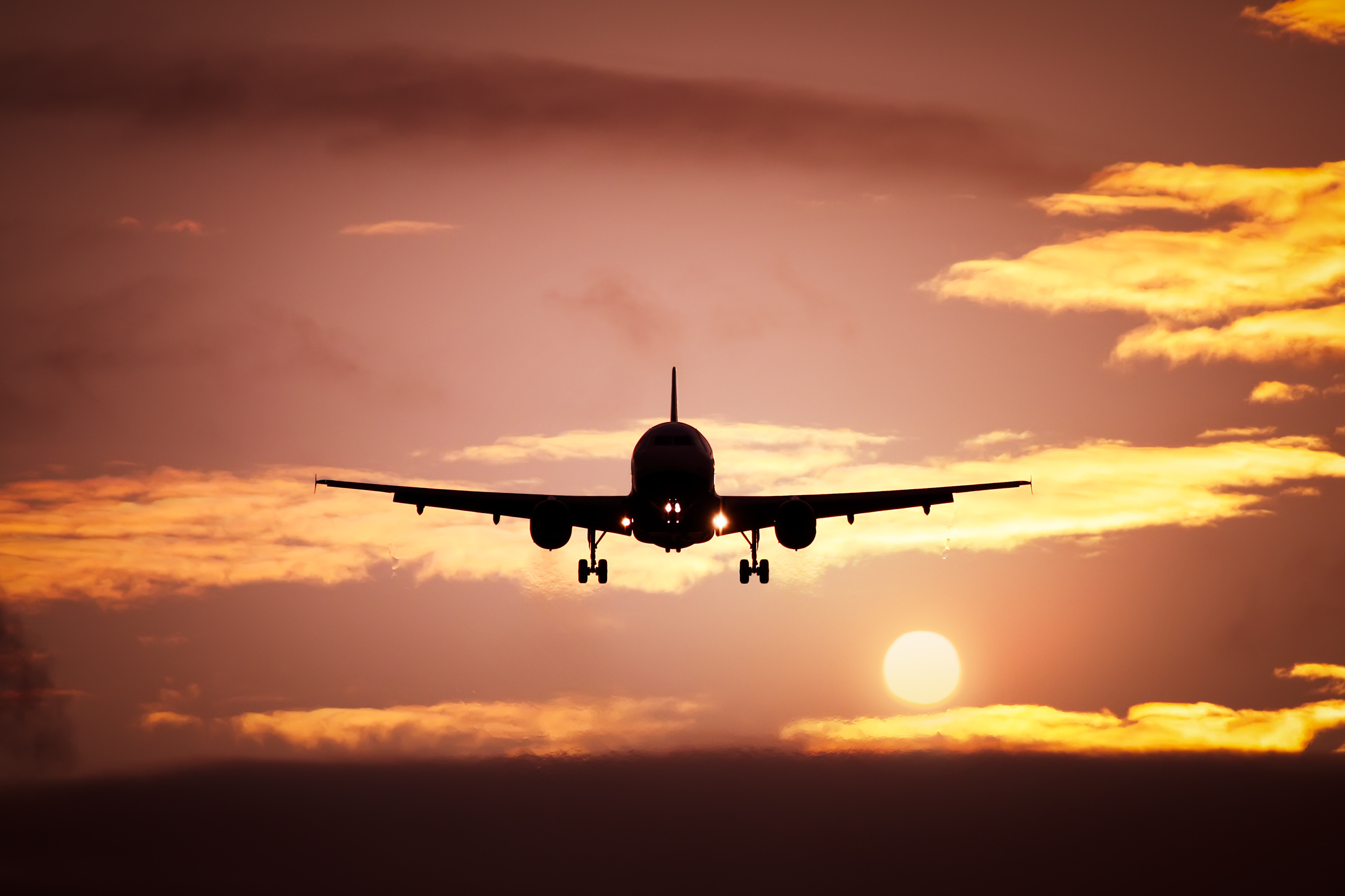 Silhouette of a passenger airplane landing against a vibrant sunset sky