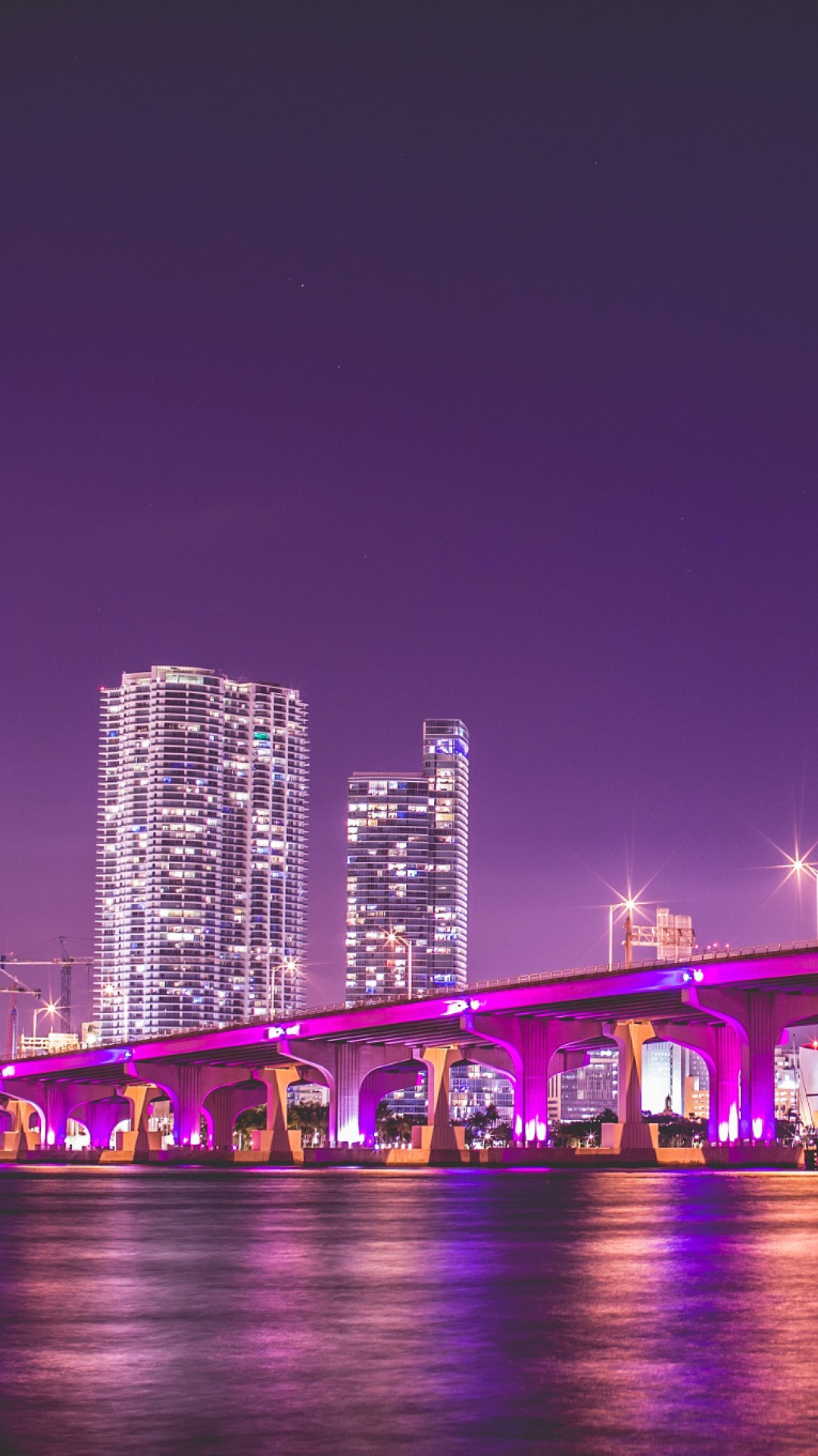 Vibrant Miami cityscape at night with a bridge illuminated in pink, modern skyscrapers, and a purple sky