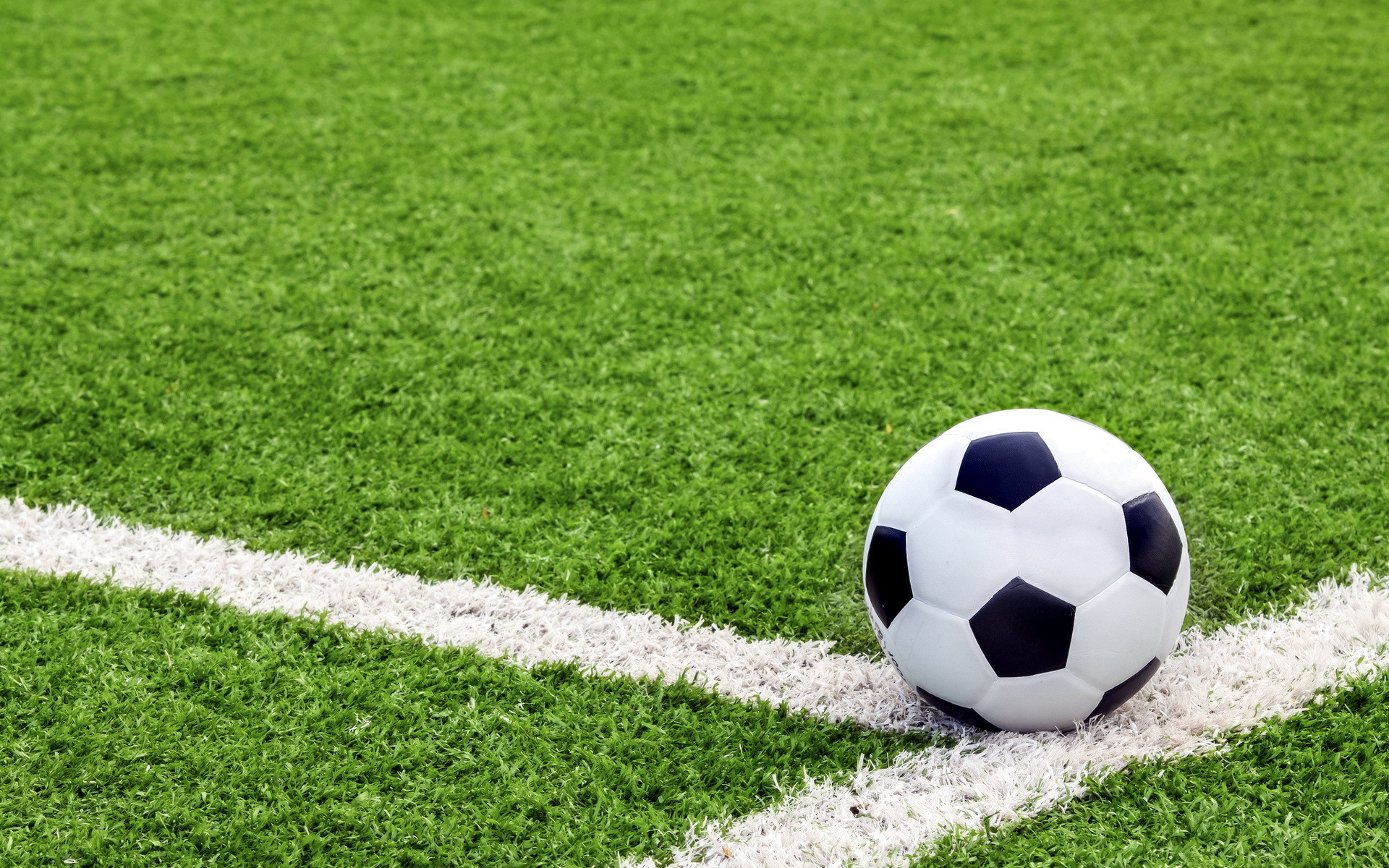 A classic black and white soccer ball sits on the vibrant green turf of a soccer field, resting against the crisp white boundary line. This image evokes the spirit of the beautiful game, perfect for soccer enthusiasts