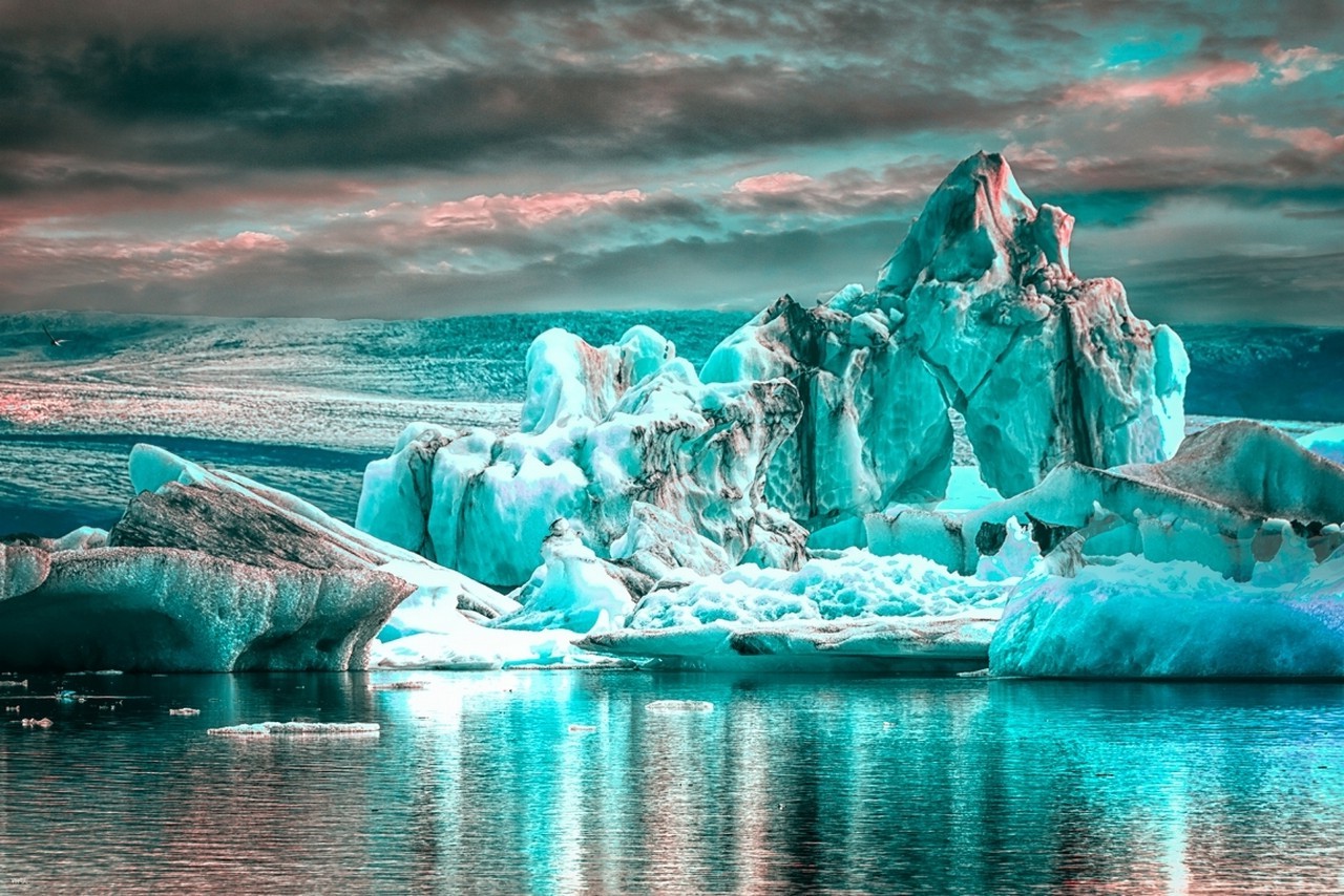 Stunning turquoise icebergs floating in a serene glacial lagoon, reflecting the dramatic colors of the sky above
