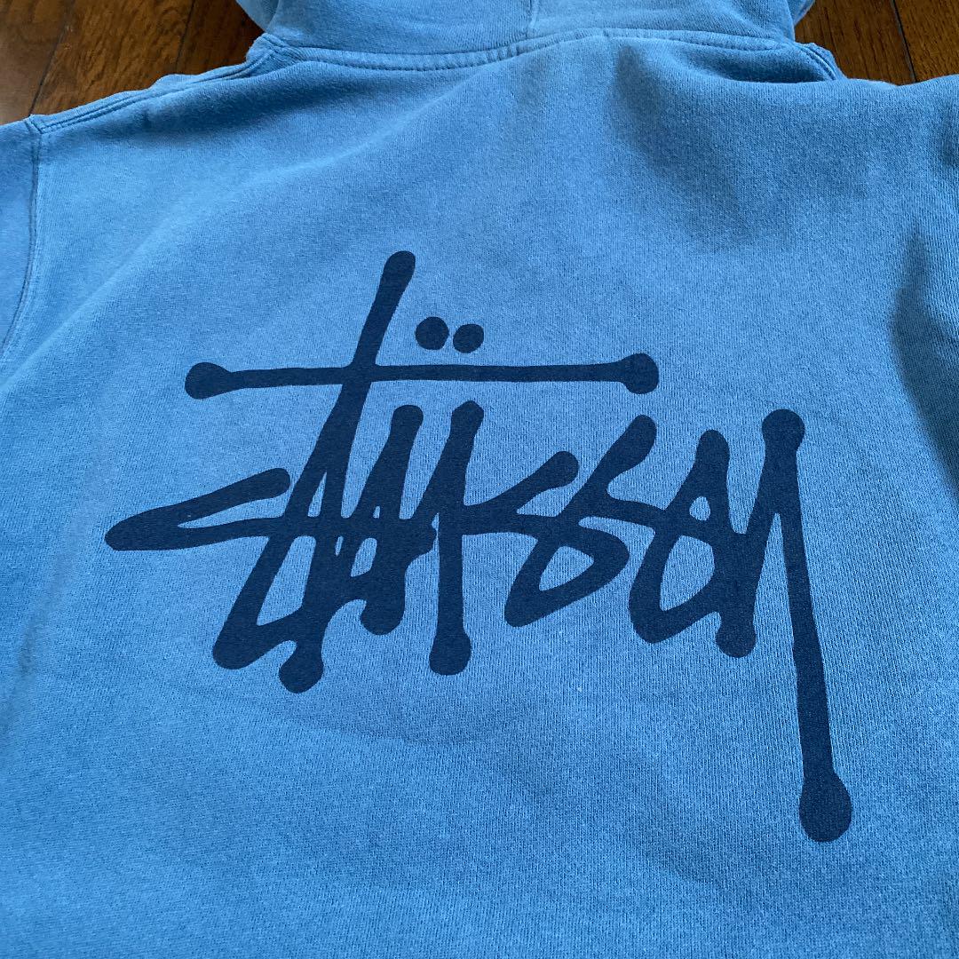 Close-up of a blue Stussy hoodie featuring the iconic Stussy logo on the back