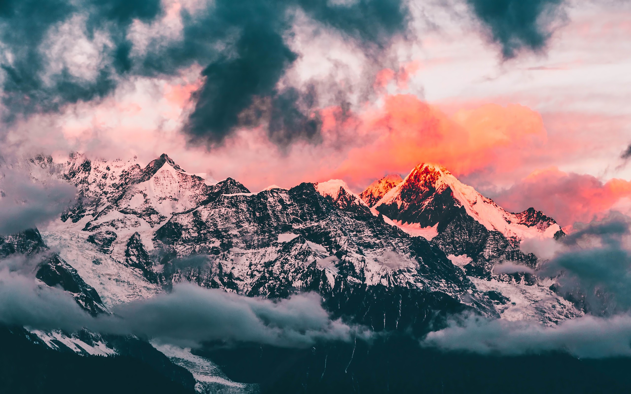 Majestic snow-capped mountain range at sunset, with vibrant pink and orange hues illuminating the peaks and dramatic clouds overhead
