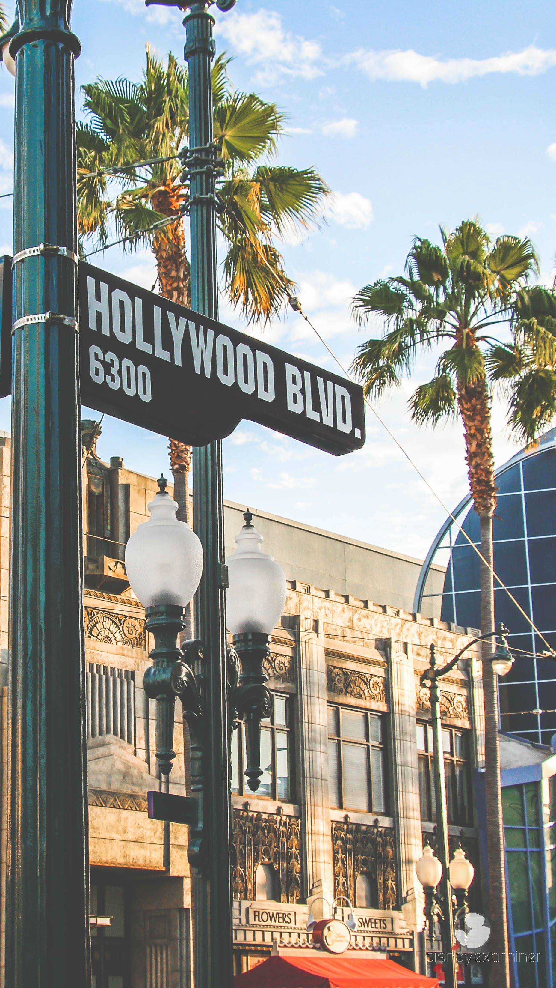 A close-up view of the Hollywood Boulevard street sign, with palm trees and the iconic architecture of Hollywood in the background