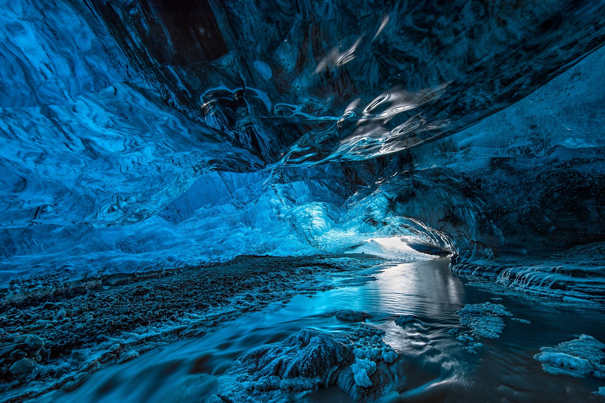A breathtaking view inside a vibrant blue ice cave, with a flowing stream reflecting the icy ceiling